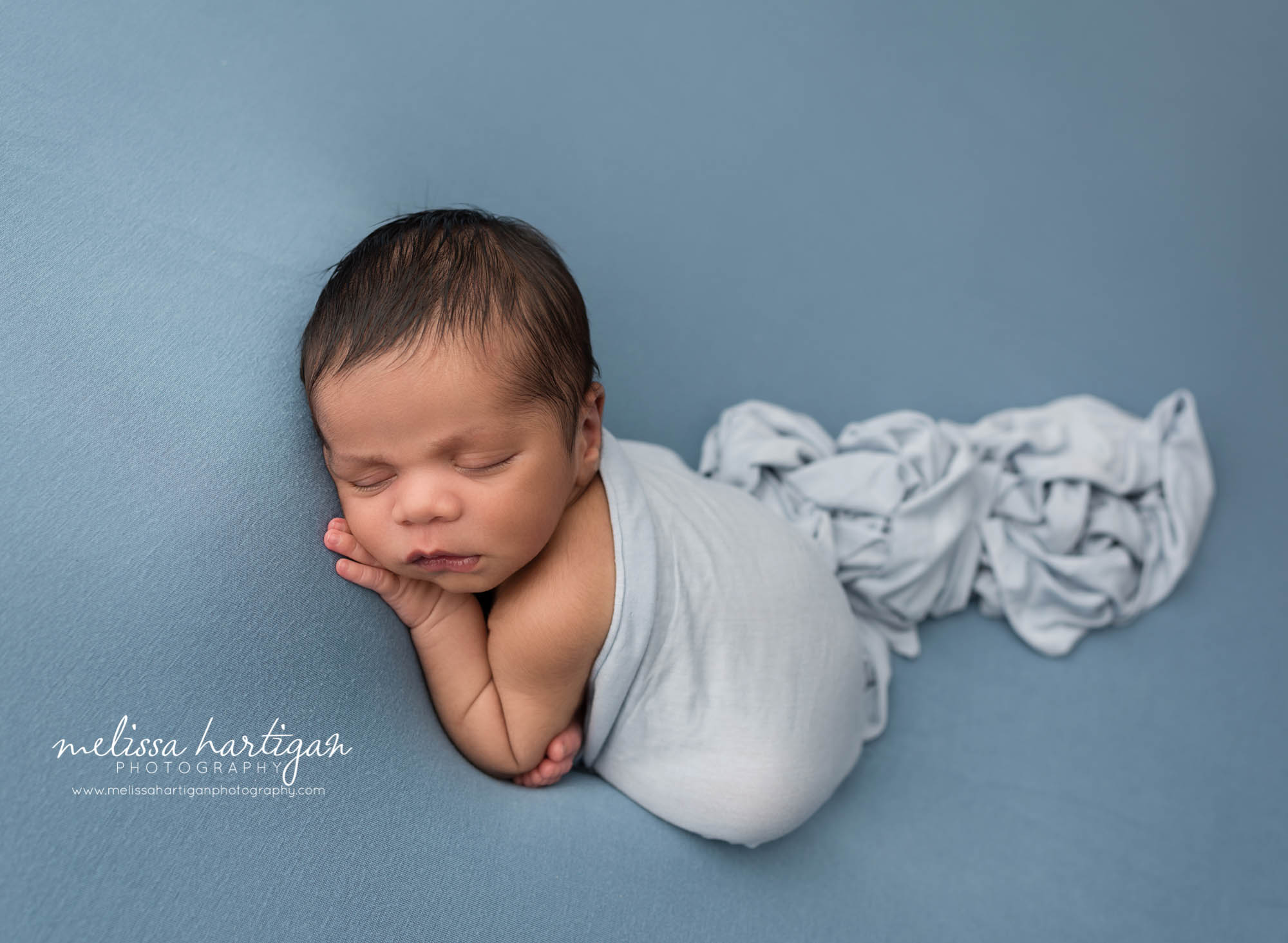 newborn baby boy posed on blue backdrop with light blue fabric draping over him