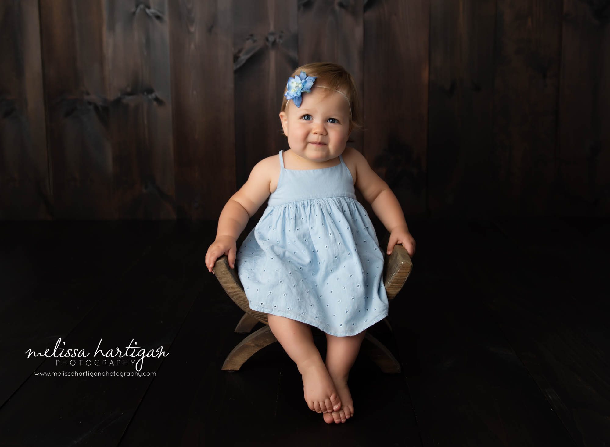baby girl wearing light blue dress sitting on wooden bench in milestone photography session