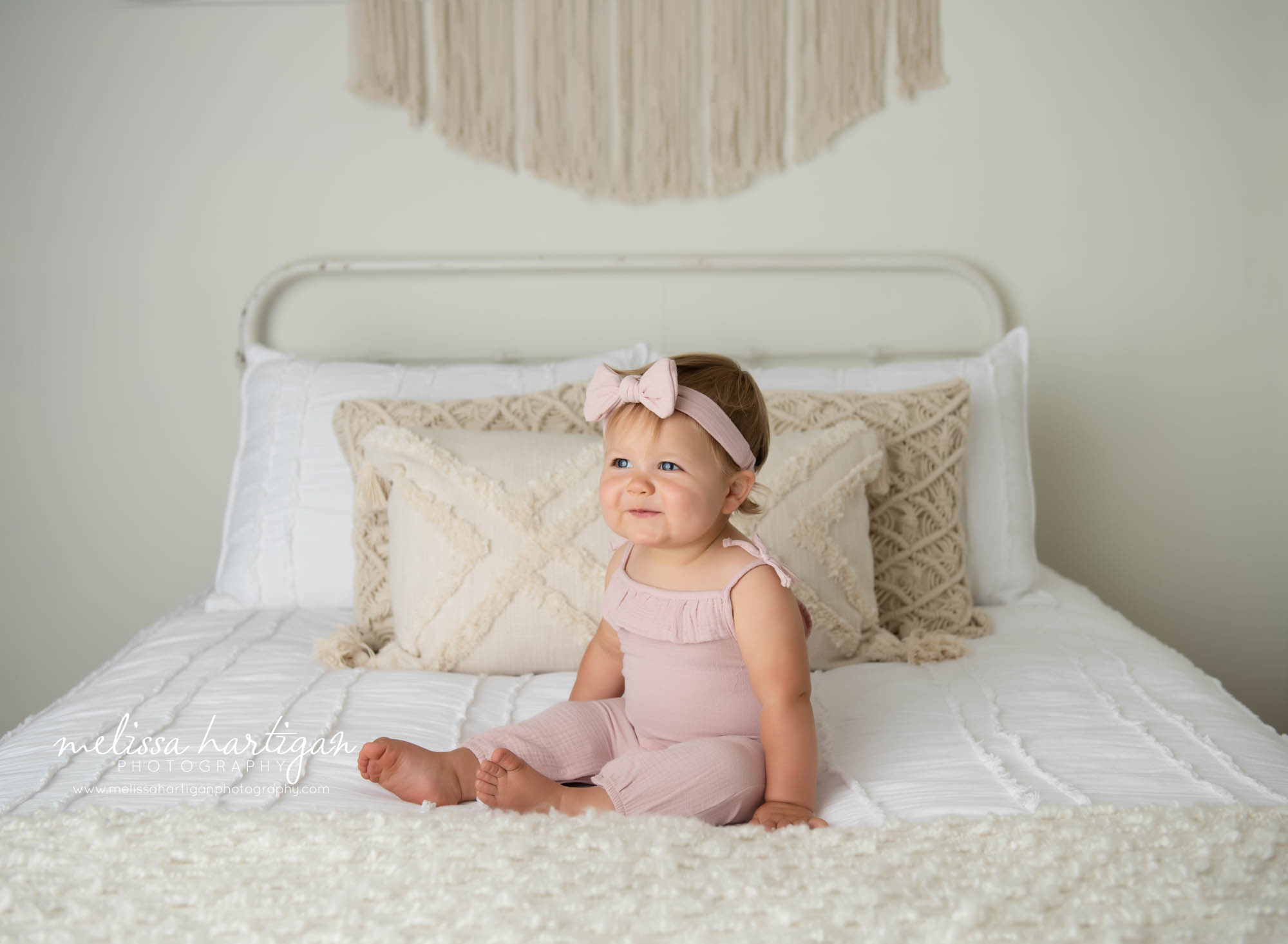 baby girl sitting on boho styled bed wearing pink outfit and bow headband