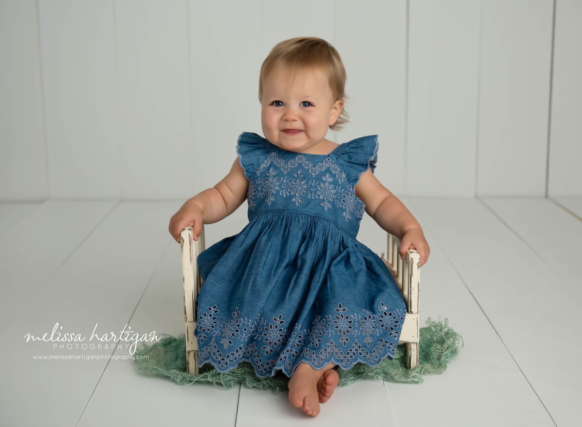 baby girl sitting on wooden bed prop wearing blue dress happy girl