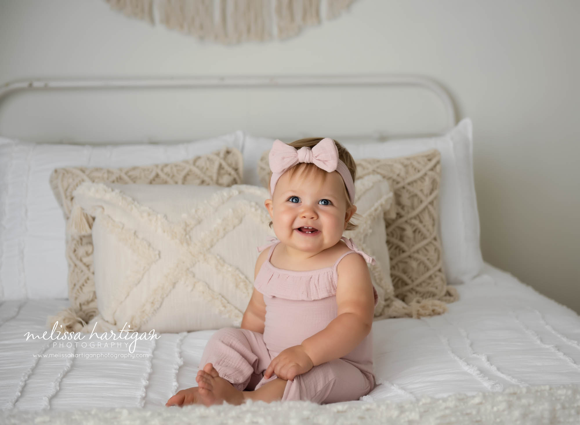 happy baby girl sitting on bed wearing pink baby girl outfit with matching bow headband hartford county ct baby photography
