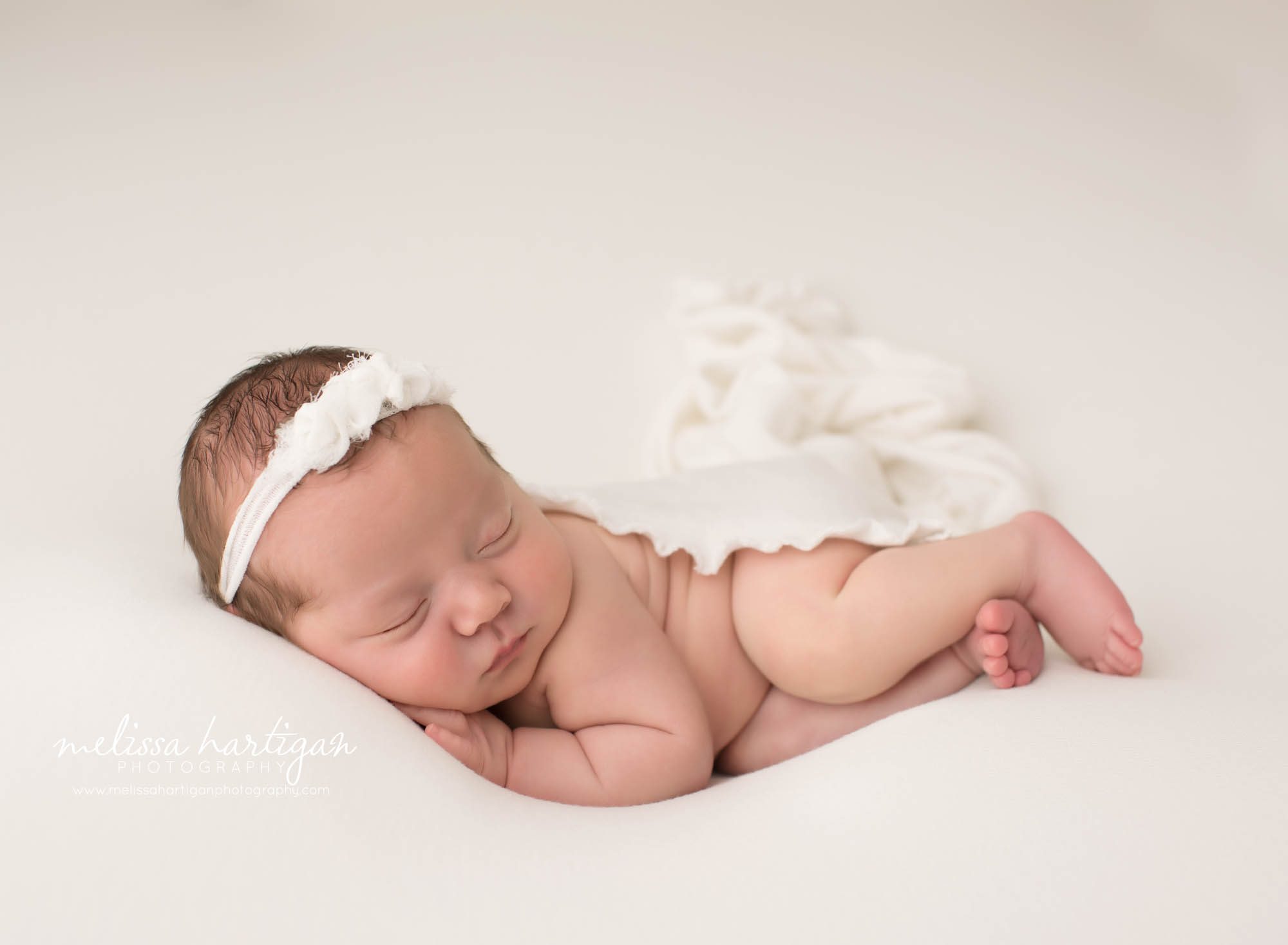 newborn baby girl posed on side with cream knitted layer draped over he backside