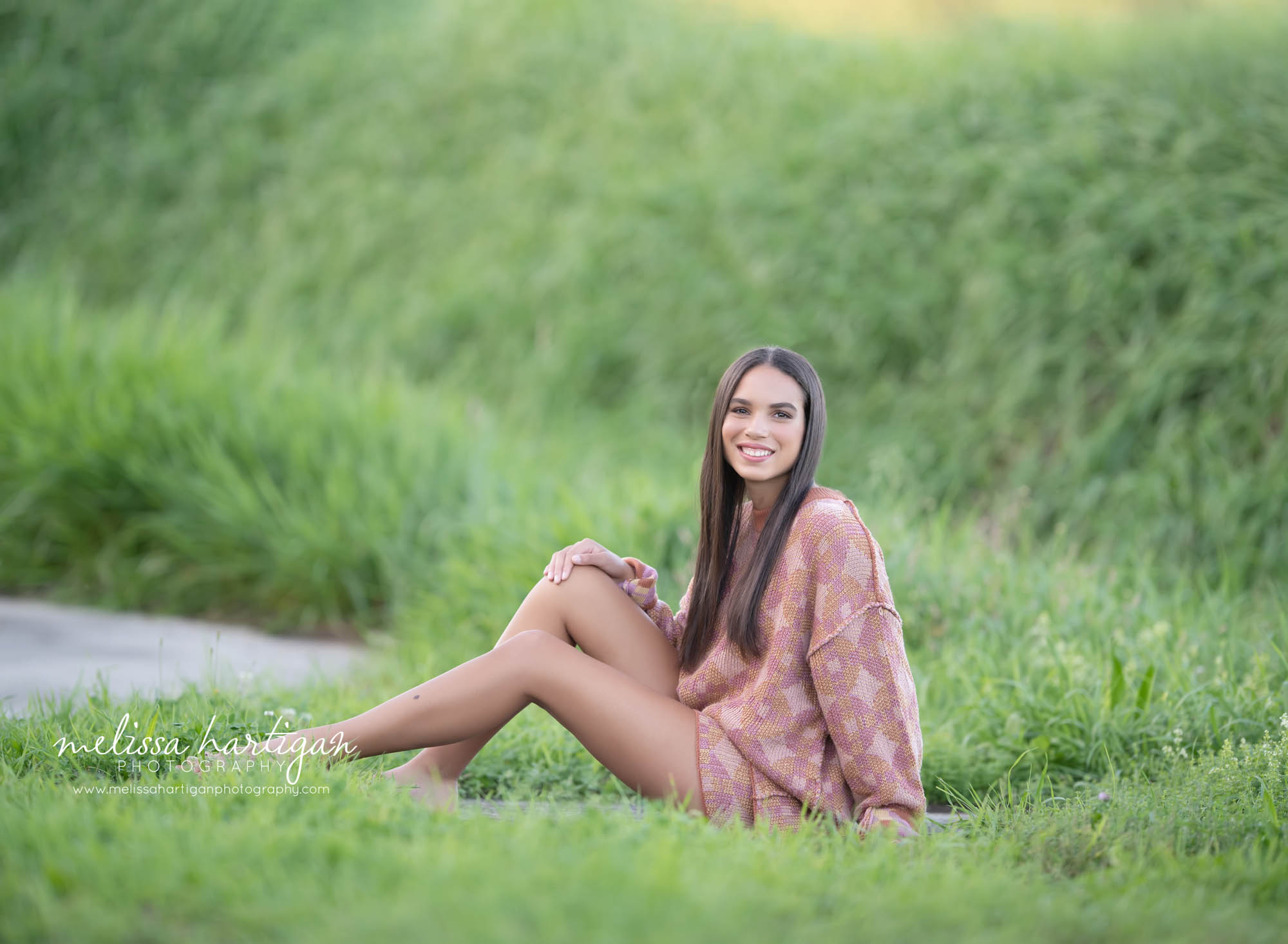 girl sitting in grass looking at camera happy senior portrait photogapher