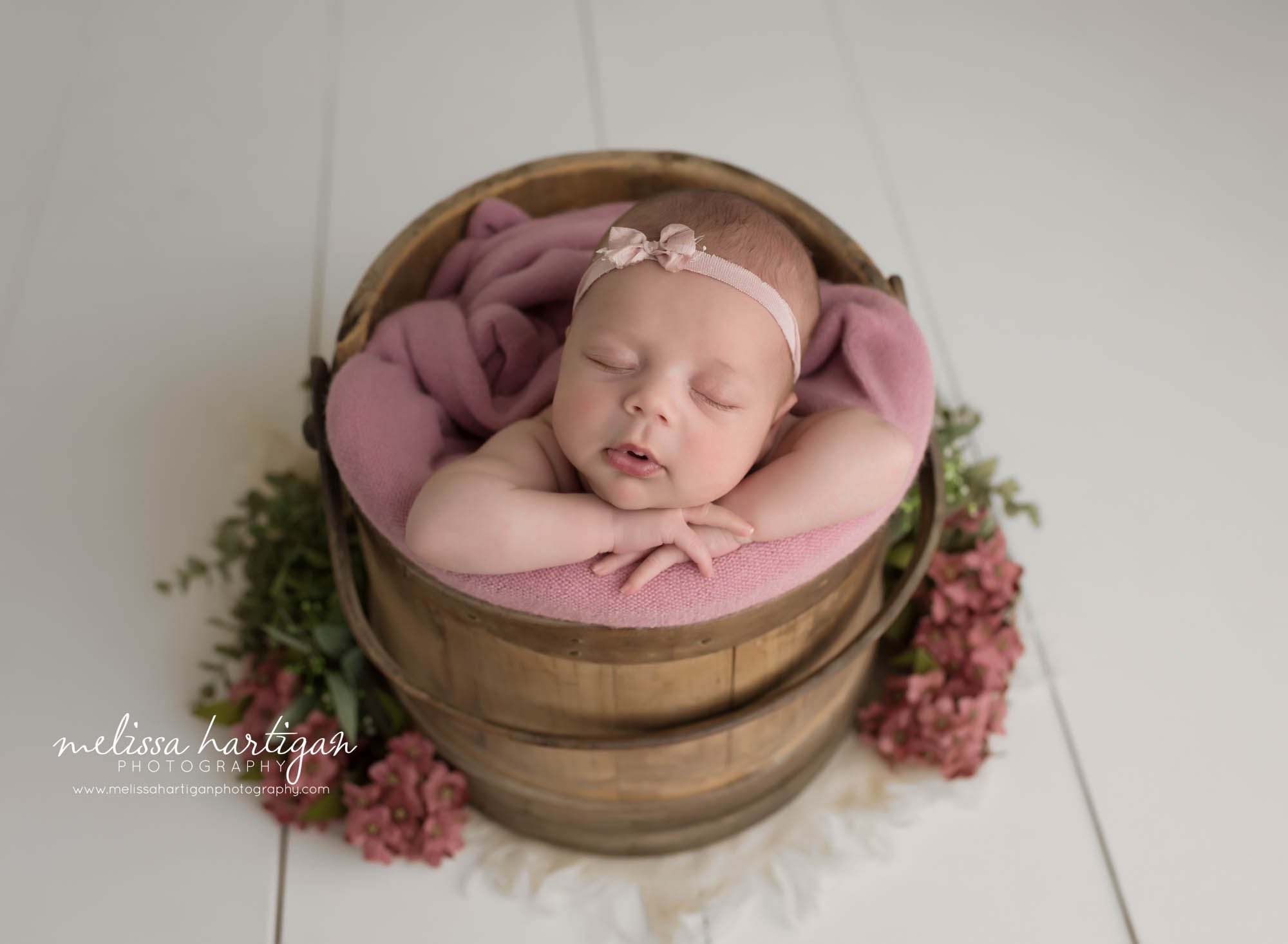 newborn baby girl posed in wooden bucket with rose pink layer and pink headband