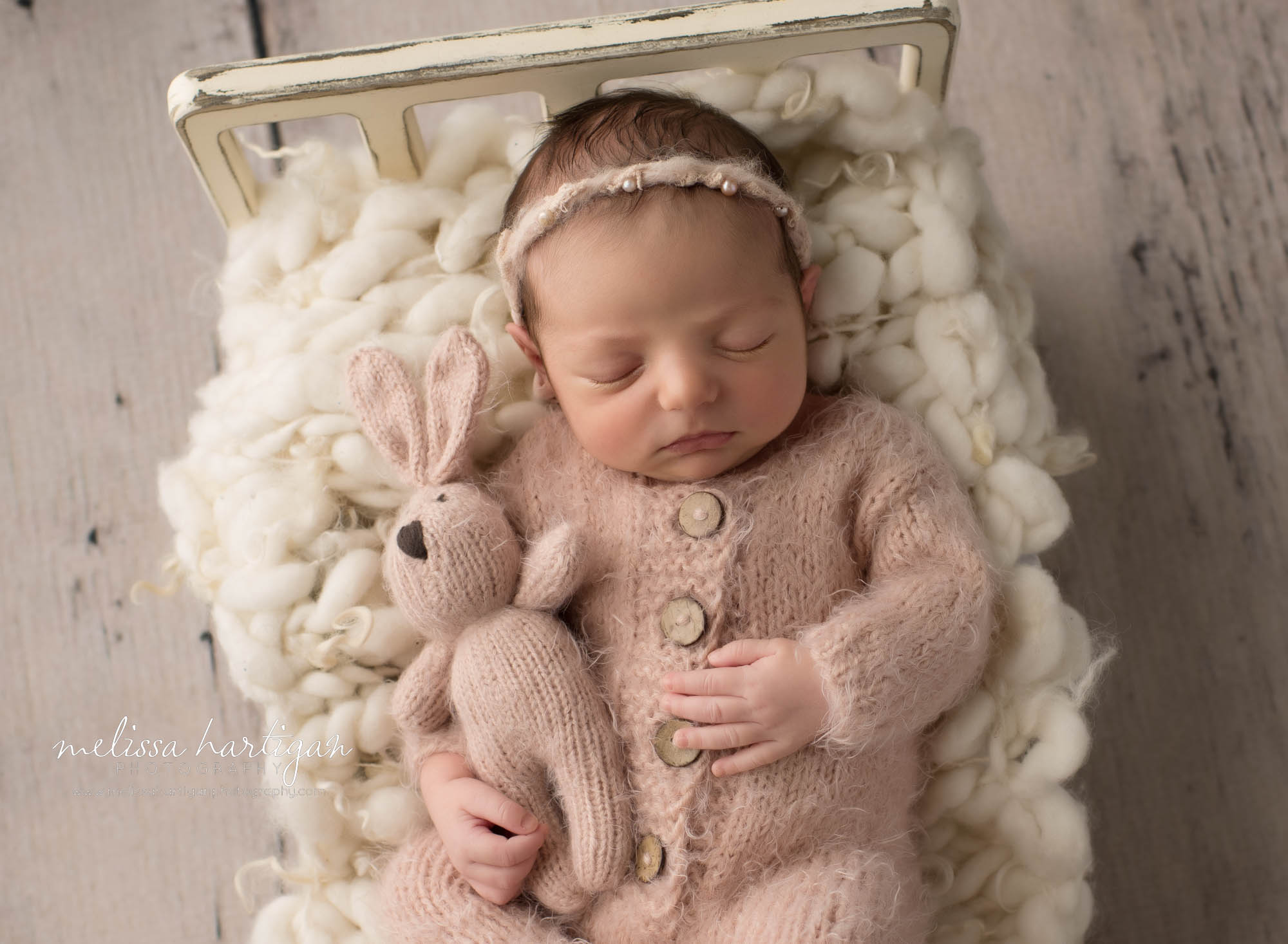 newborn baby girl posed on bed prop holding pink knitted bunny lovey