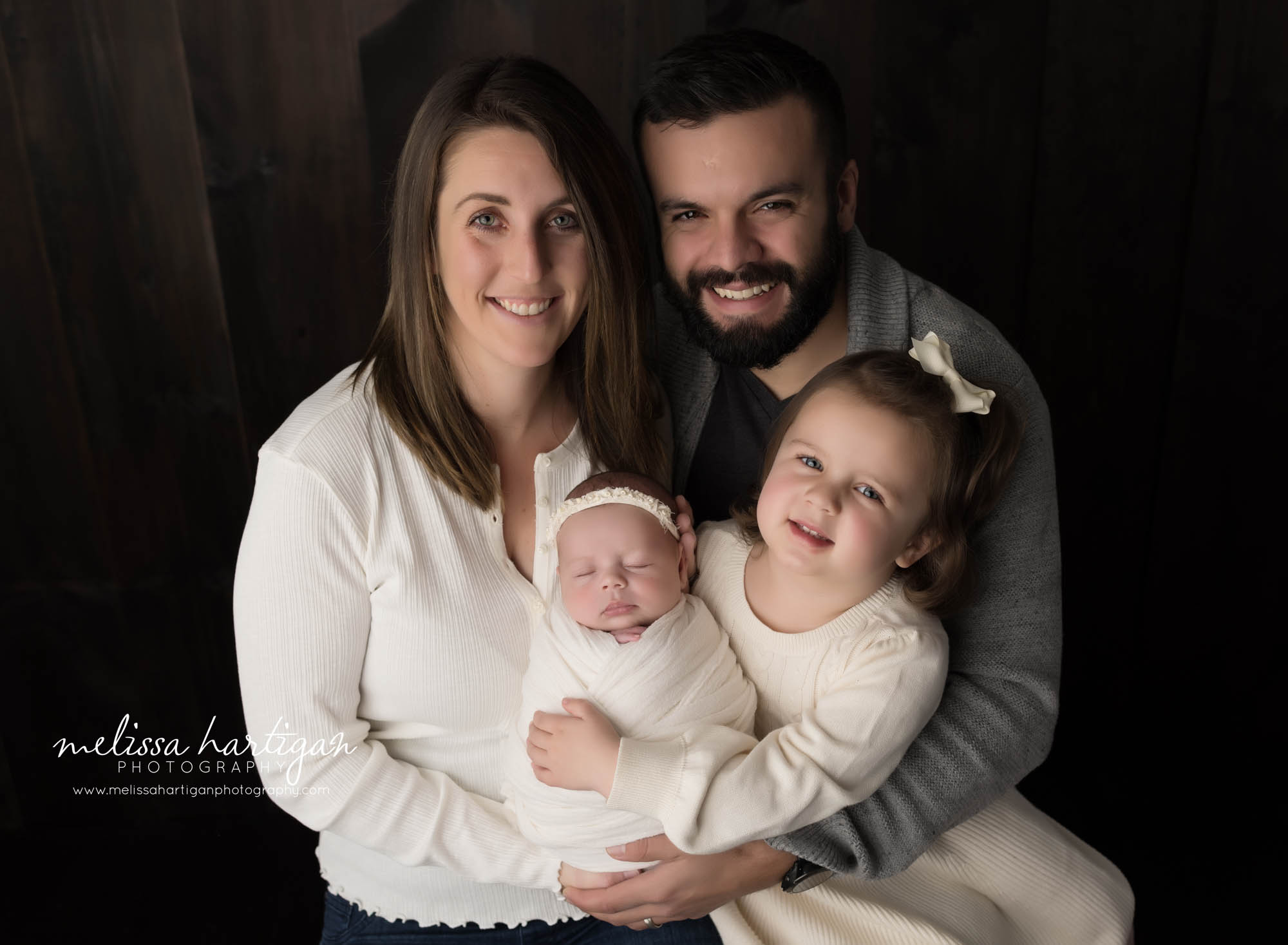 mom dad big sister holding baby sister wrapped in cream wrap in family pose newborn photography Connecticut studio