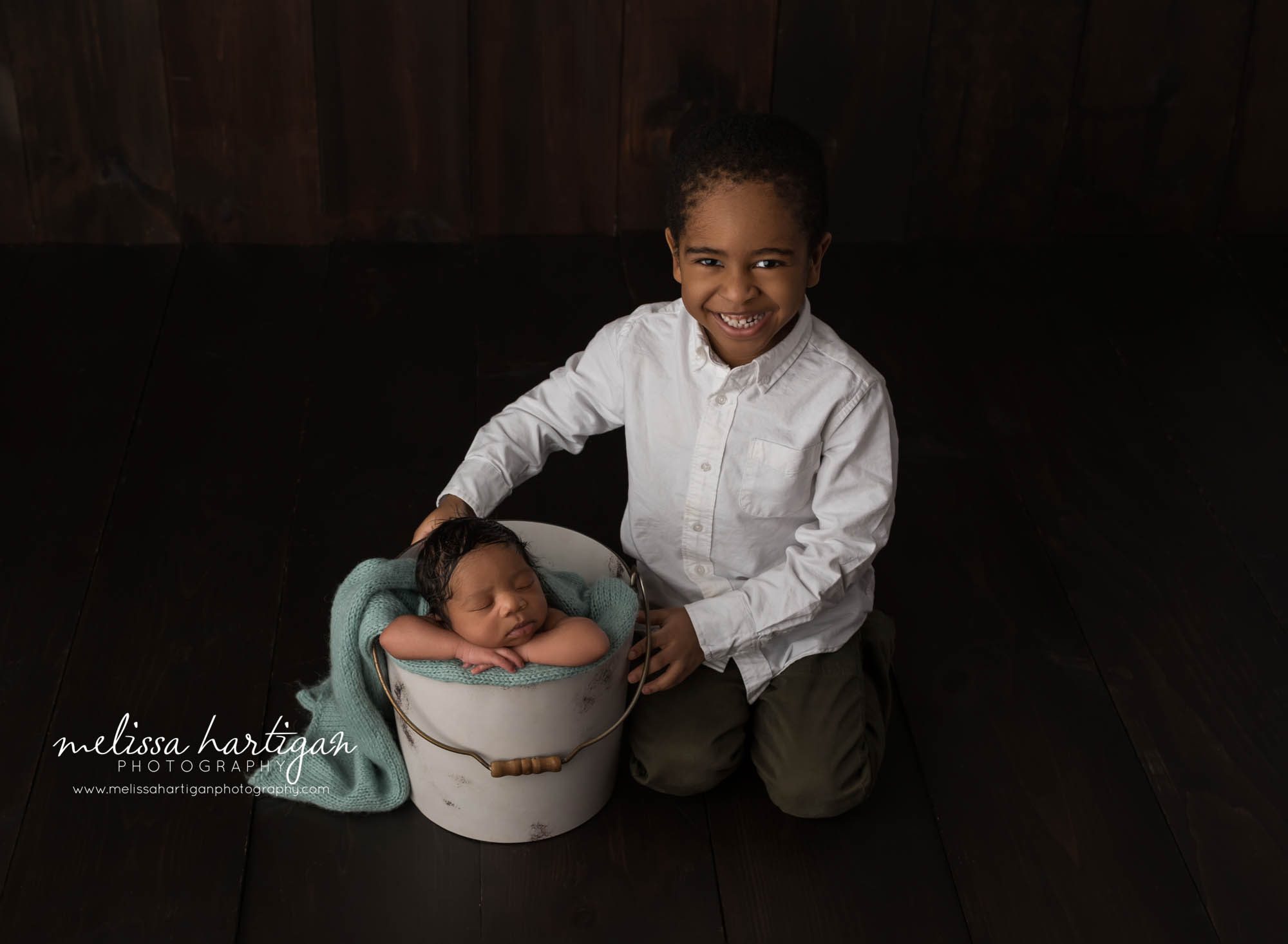 big brother sitting on floor beside baby brother posed in bucket