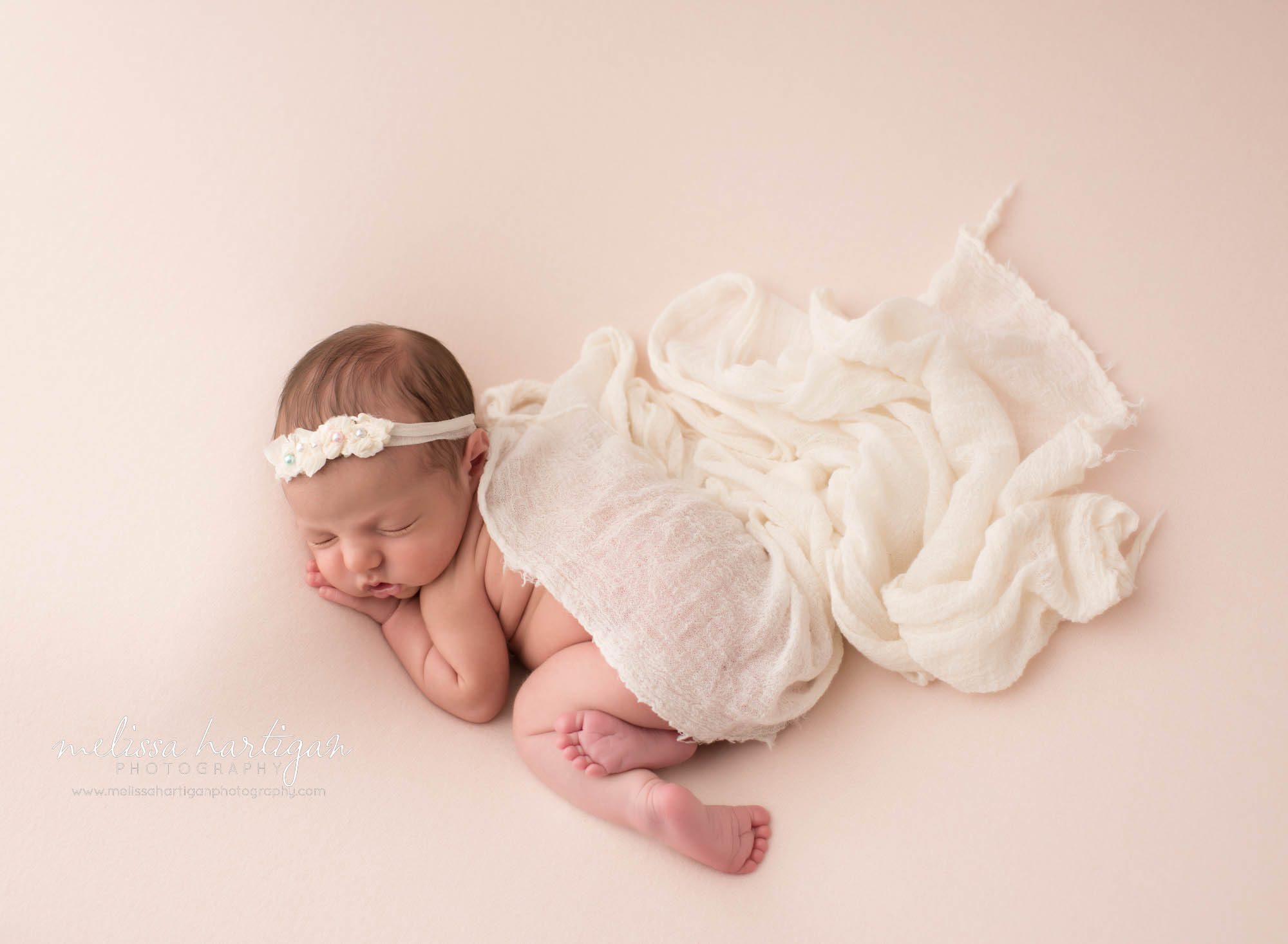 newborn baby girl posed on pink backdrop wearing cream headband and draped with cream knitted layer wrap MA newborn photography