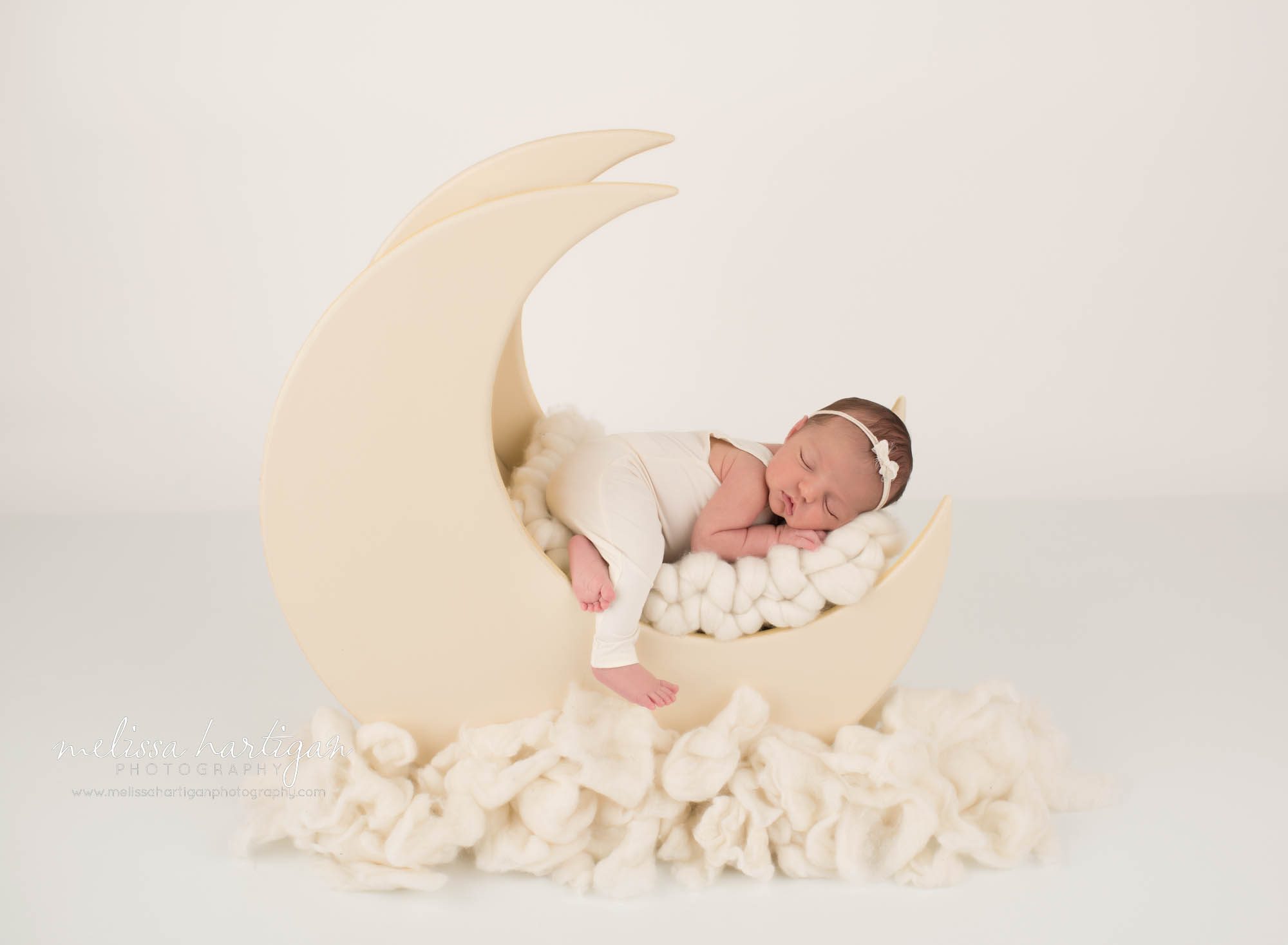 newborn baby girl posed on wooden moon prop wearing cream outfit