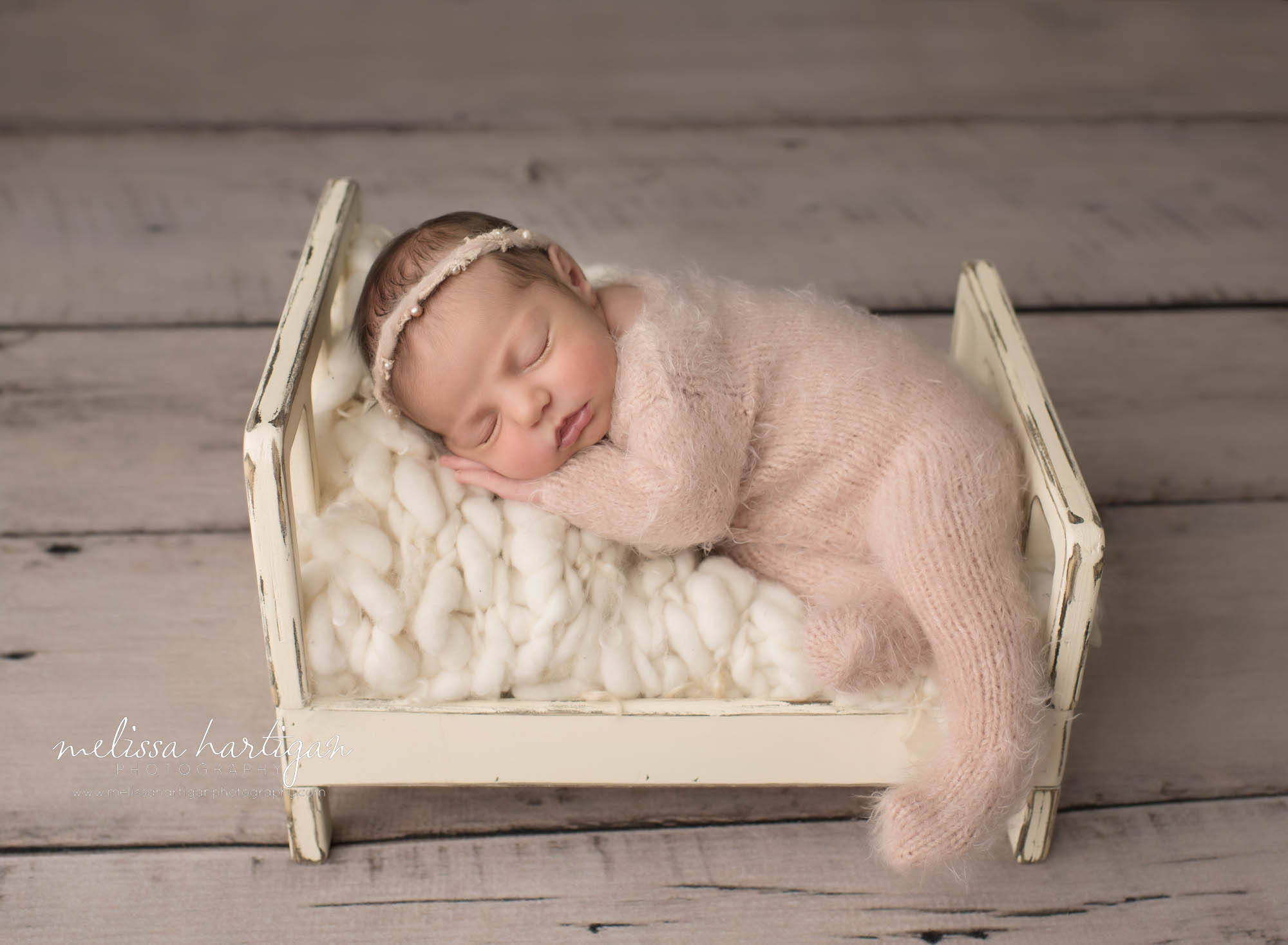 newborn baby girl pose don wooden bed prop wearing pink knitted footed sleeper