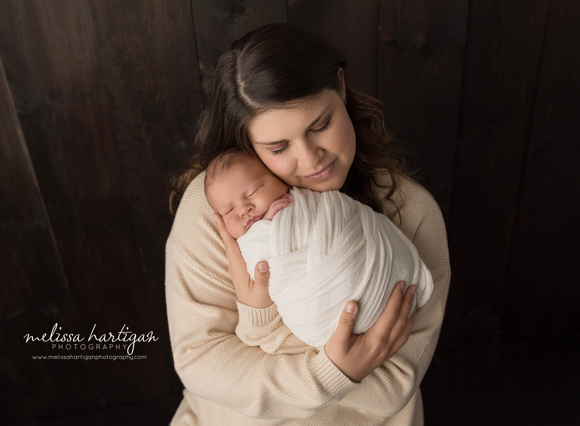 mom holding newborn son wrapped in white wrap studio parent pose