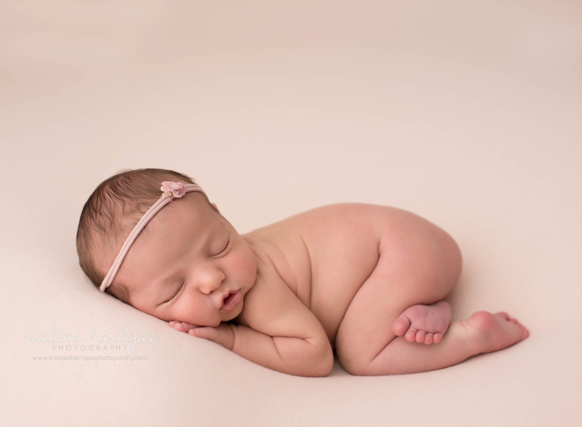 newborn baby girl posed on tummy on pink backdrop wearing pink headband newborn photographer Massachusetts
