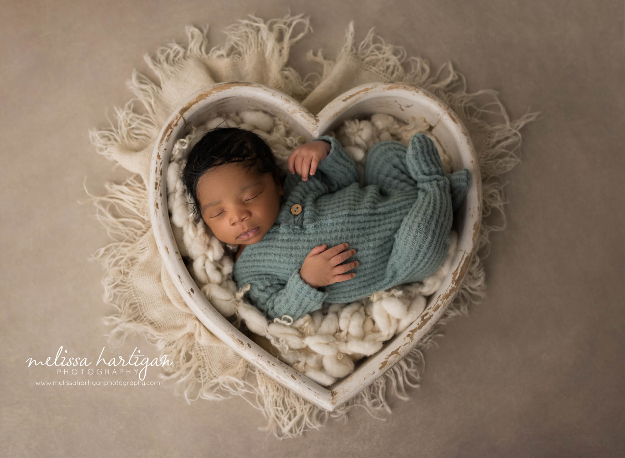 newborn baby boy posed in wooden cream heart bowl wearing soft green knitted footed sleeper