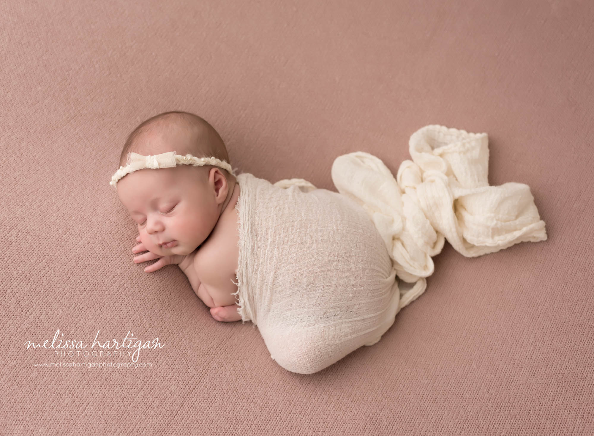 newborn baby girl posed on rose mauve colored backdrop with cream layer draped over back wearing cream headband
