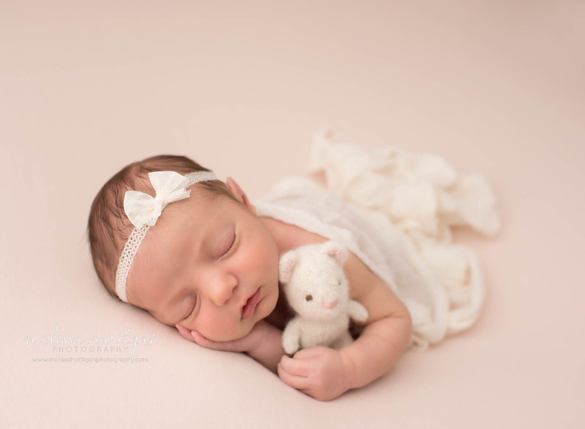 newborn baby girl posed on tummy with white knitted teddy bear