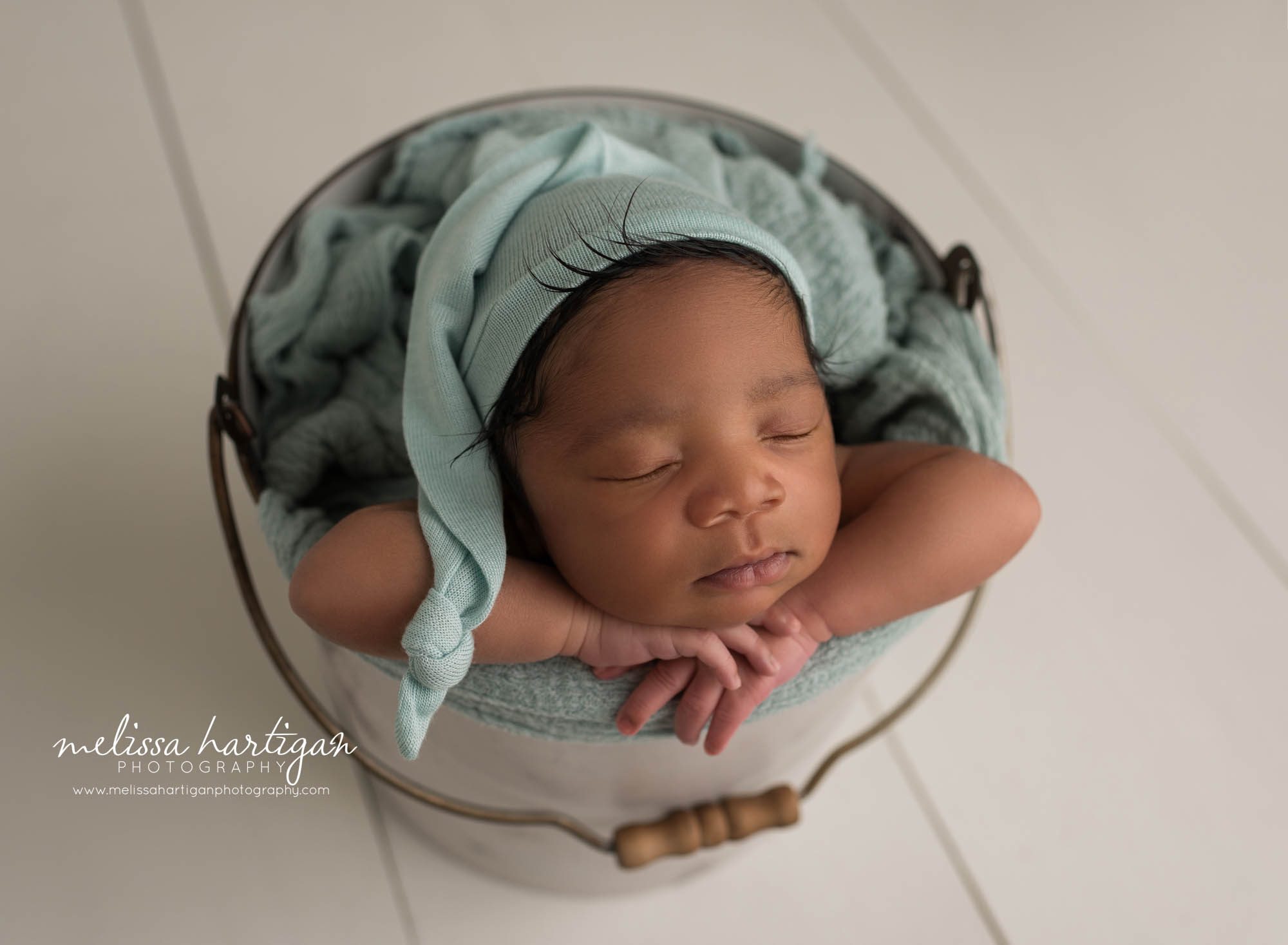 newborn baby posed in bucket wearing soft green sleepy cap