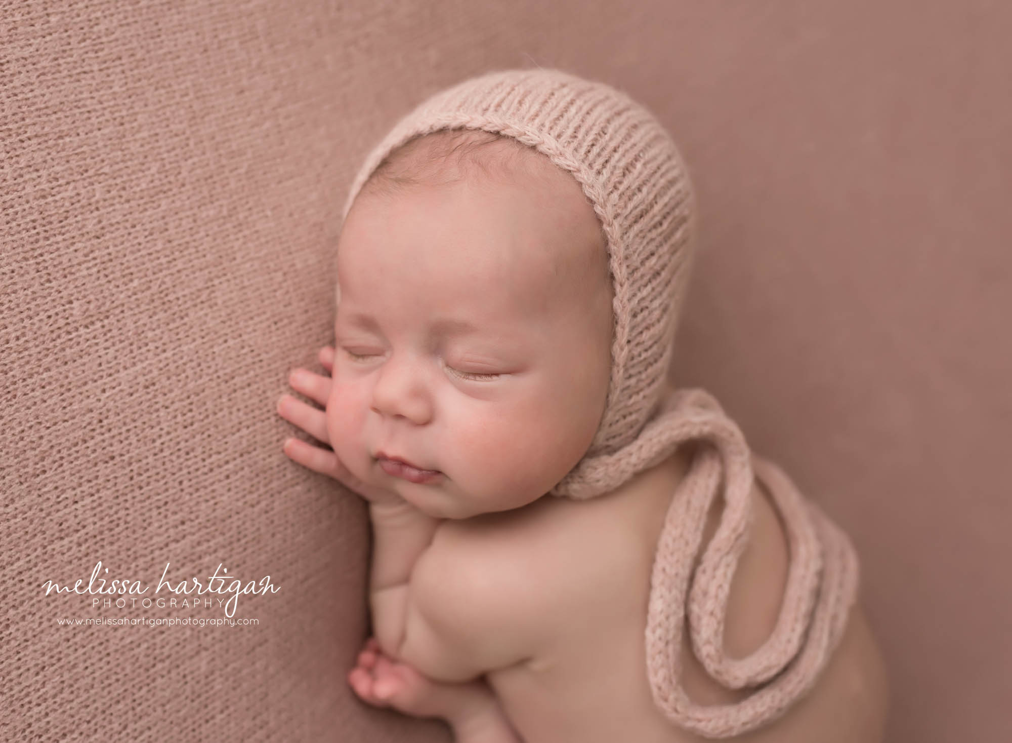 newborn baby girl posed on pink backdrop wearing knitted bonnet