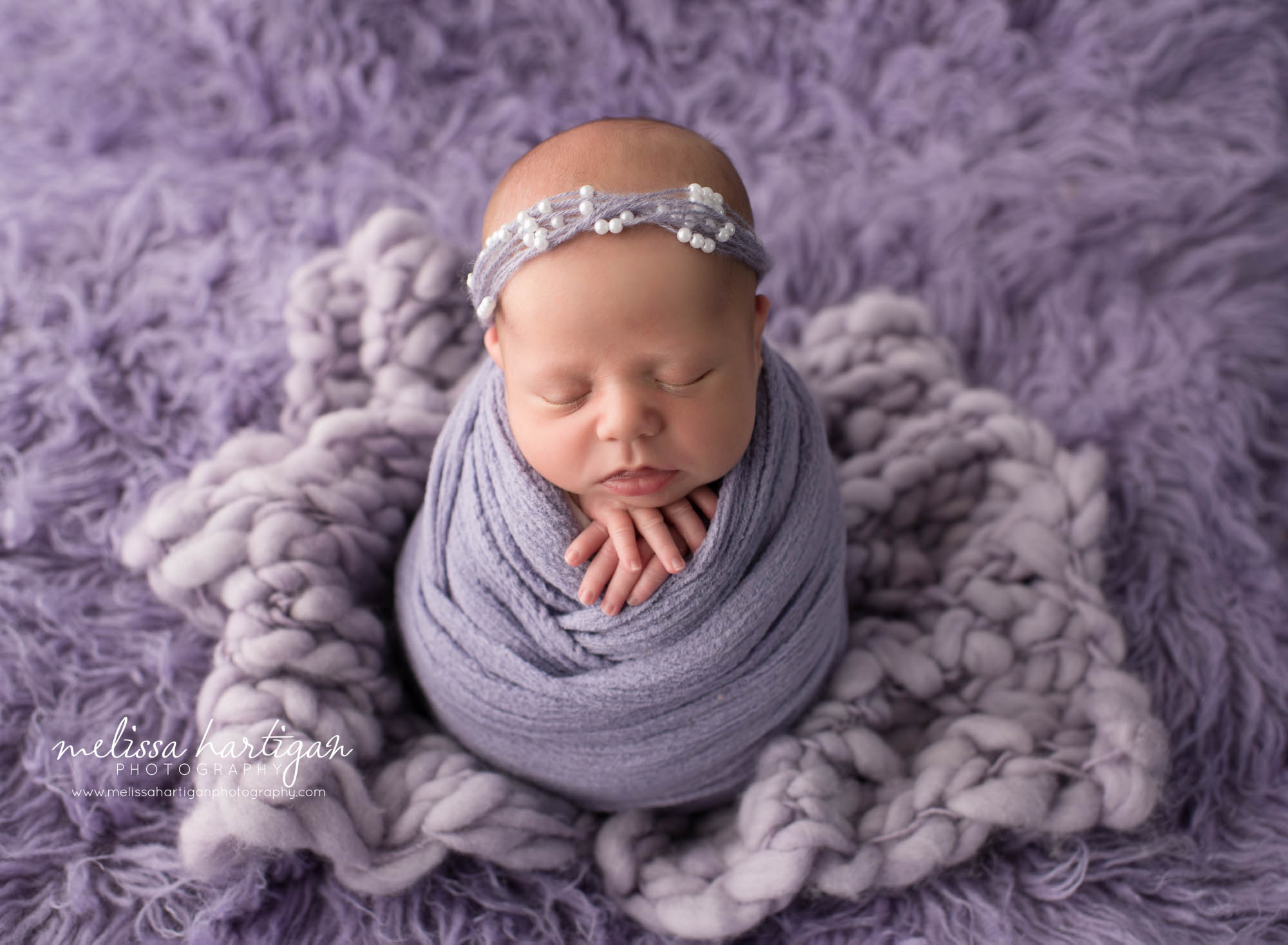newborn baby girl swaddled in purple wrap posed on purple flokati rug