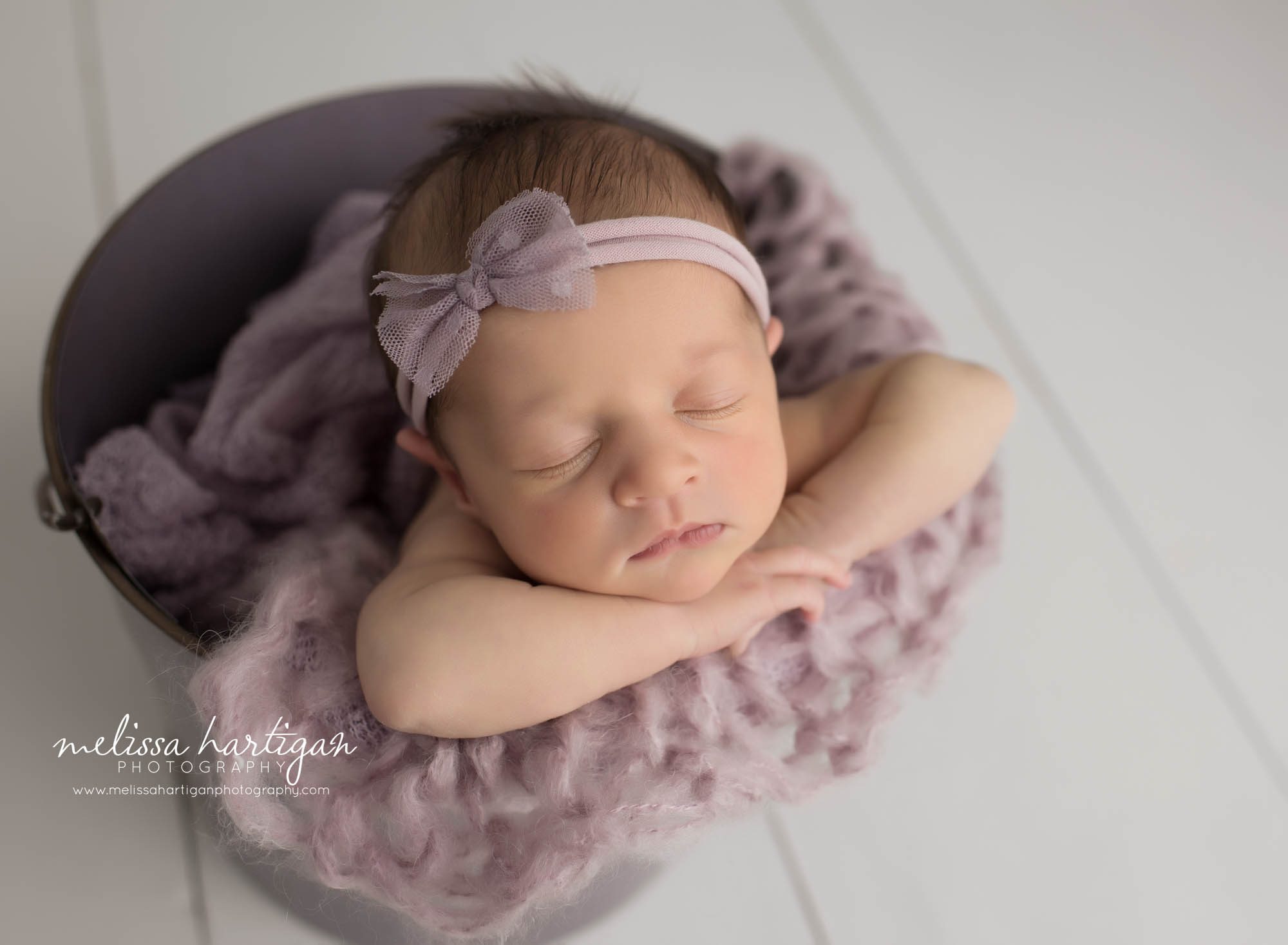 newborn baby girl posed in bucket with chin rested on her hands