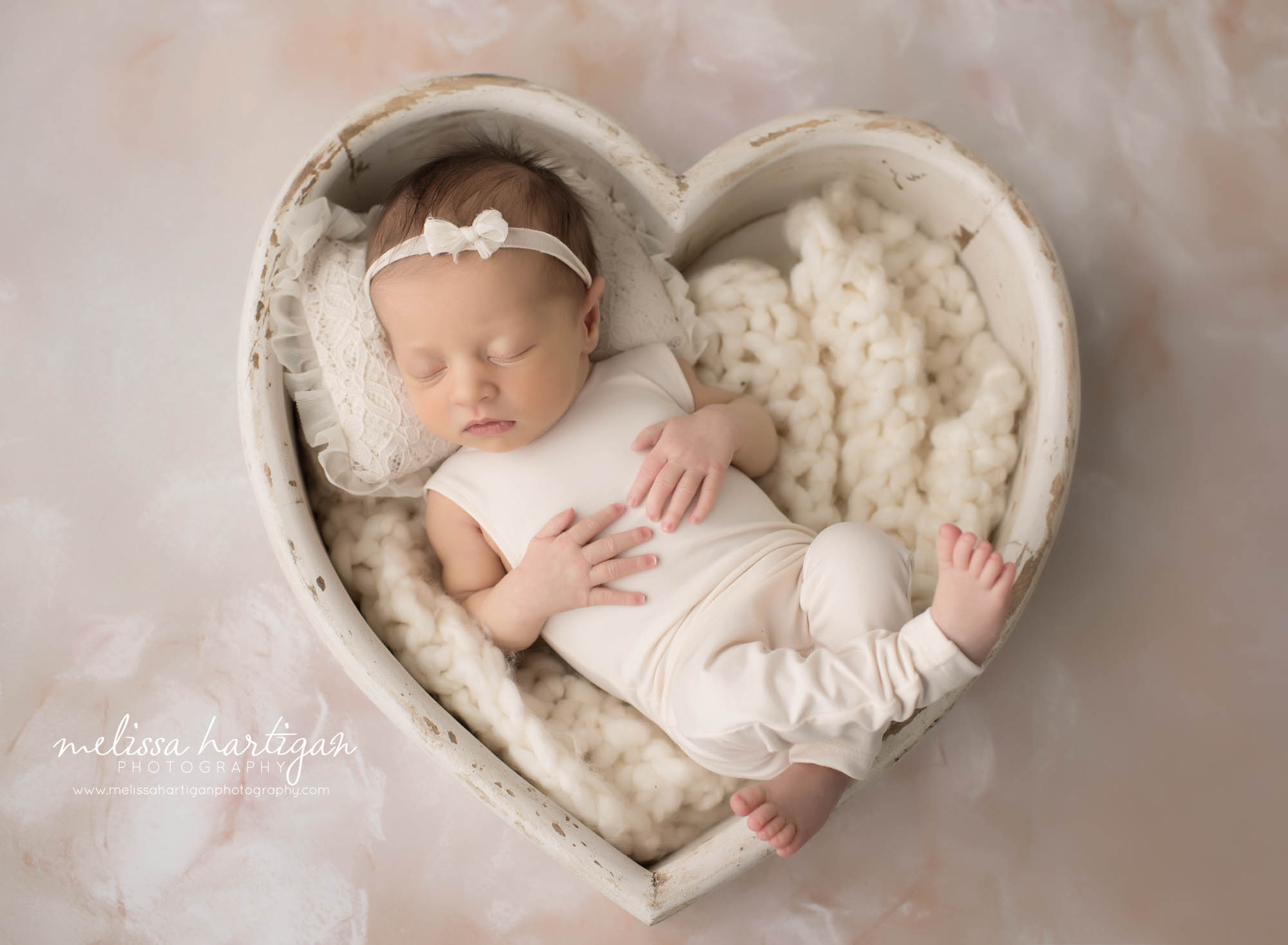 newborn baby girl posed in cream wooden heart prop wearing cream newborn girl outfit and bow headband middlesex county CT newborn photogaphy