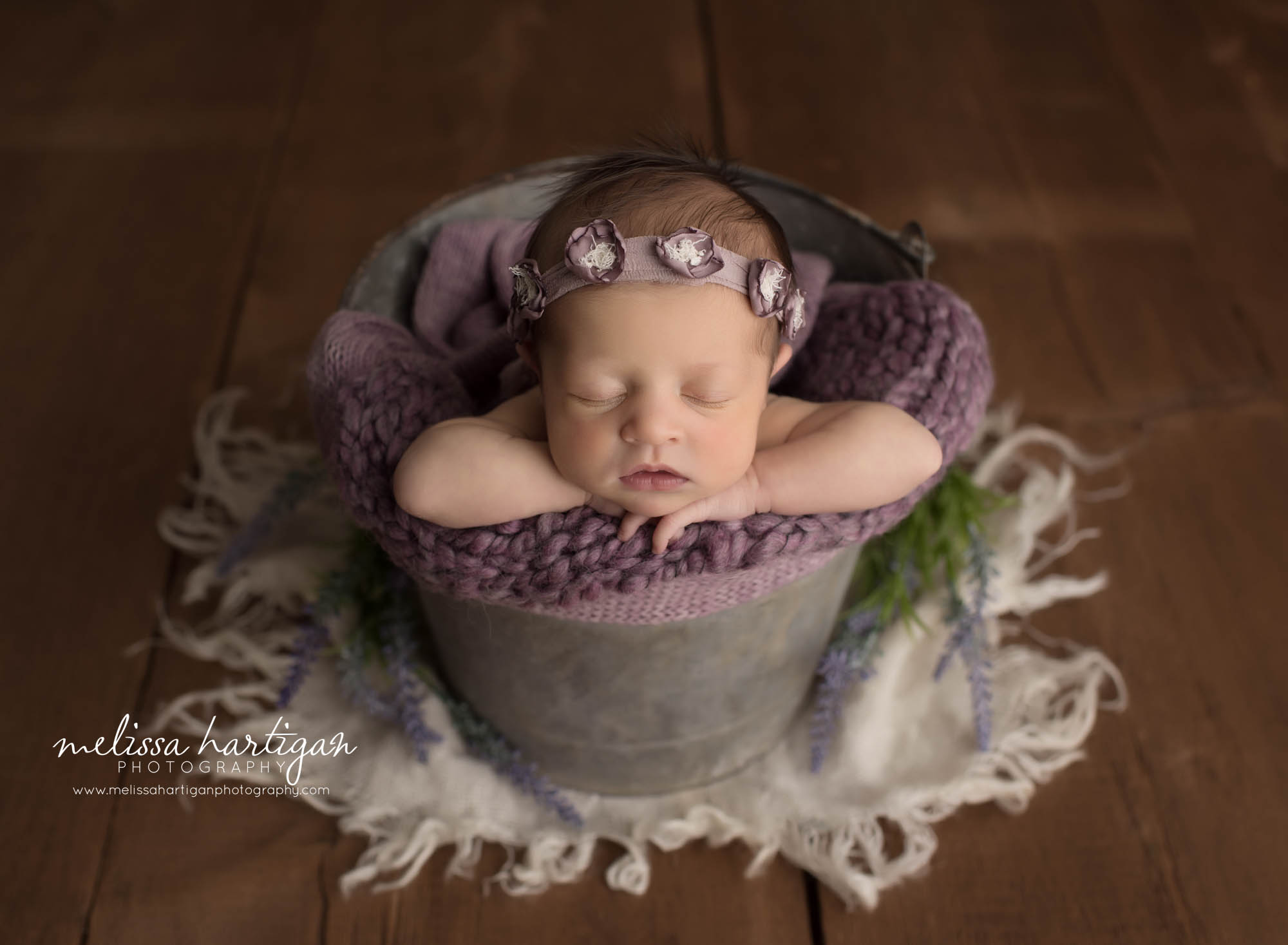 newborn baby girl posed in bucket with deep purple layer wrap and purple flower headband