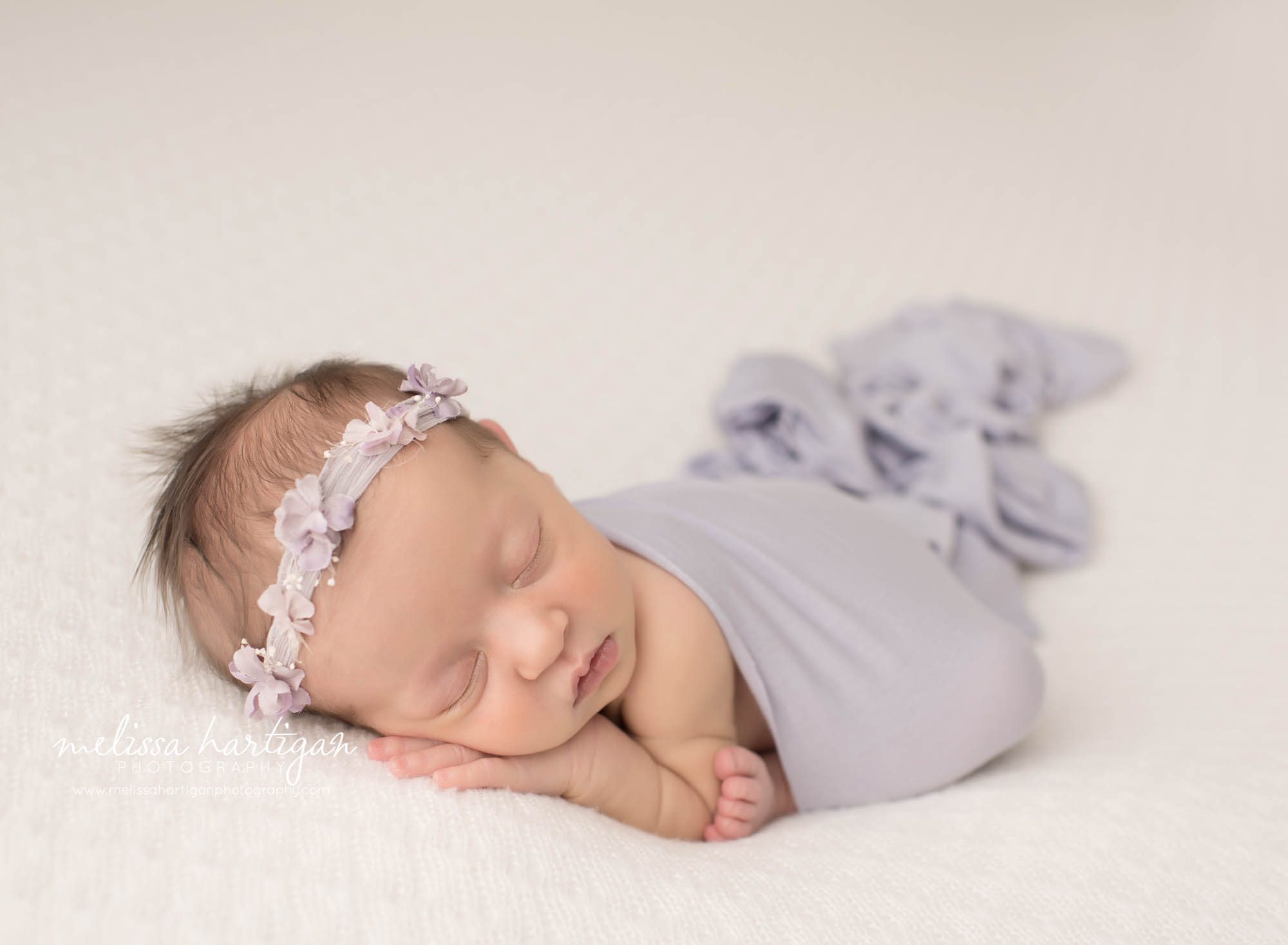 newborn baby girl posed on tummy in taco pose with purple floral headband middlesex county baby photography
