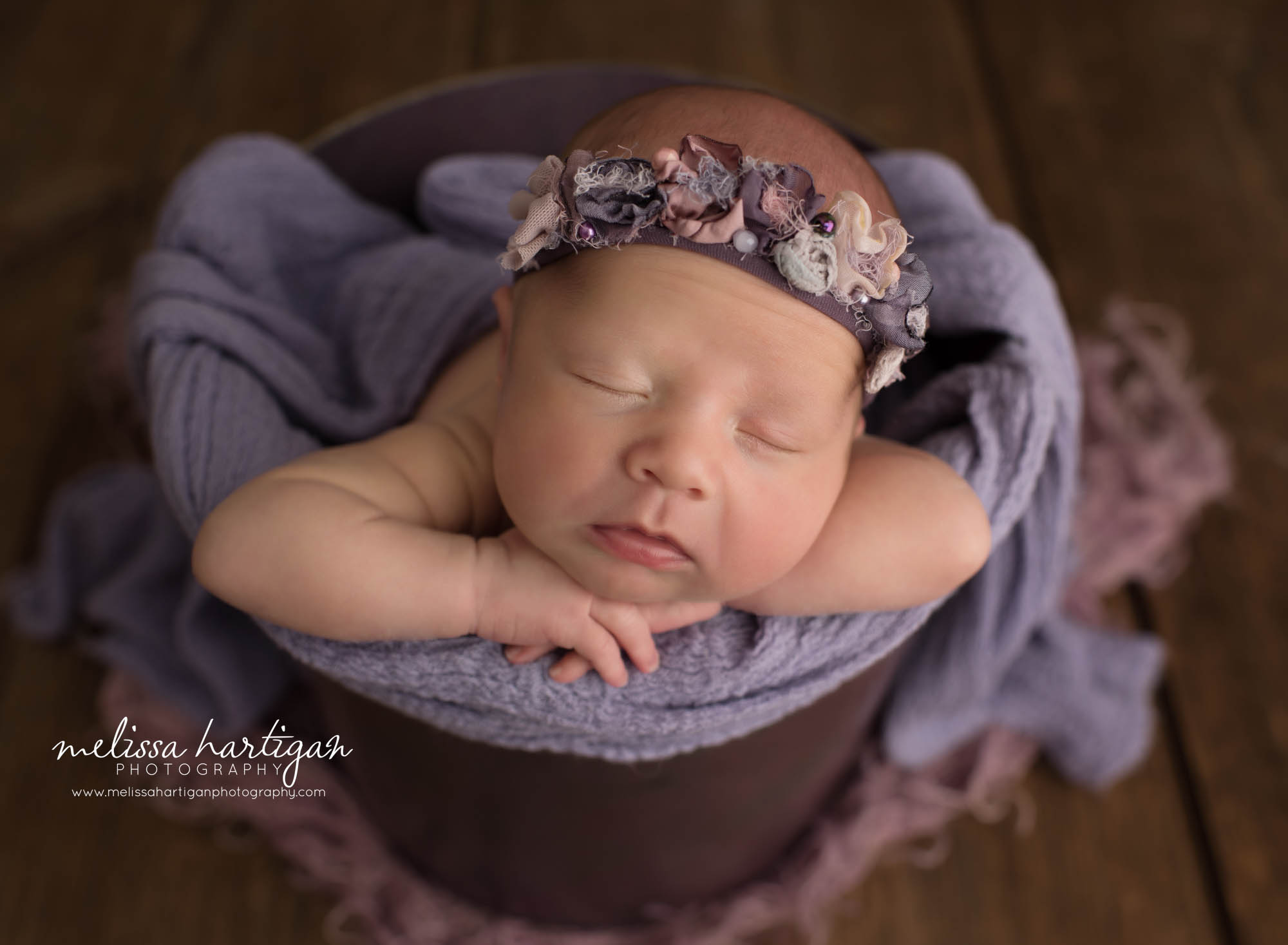 newborn baby girl posed in bucket wearing floral headband and purple draping