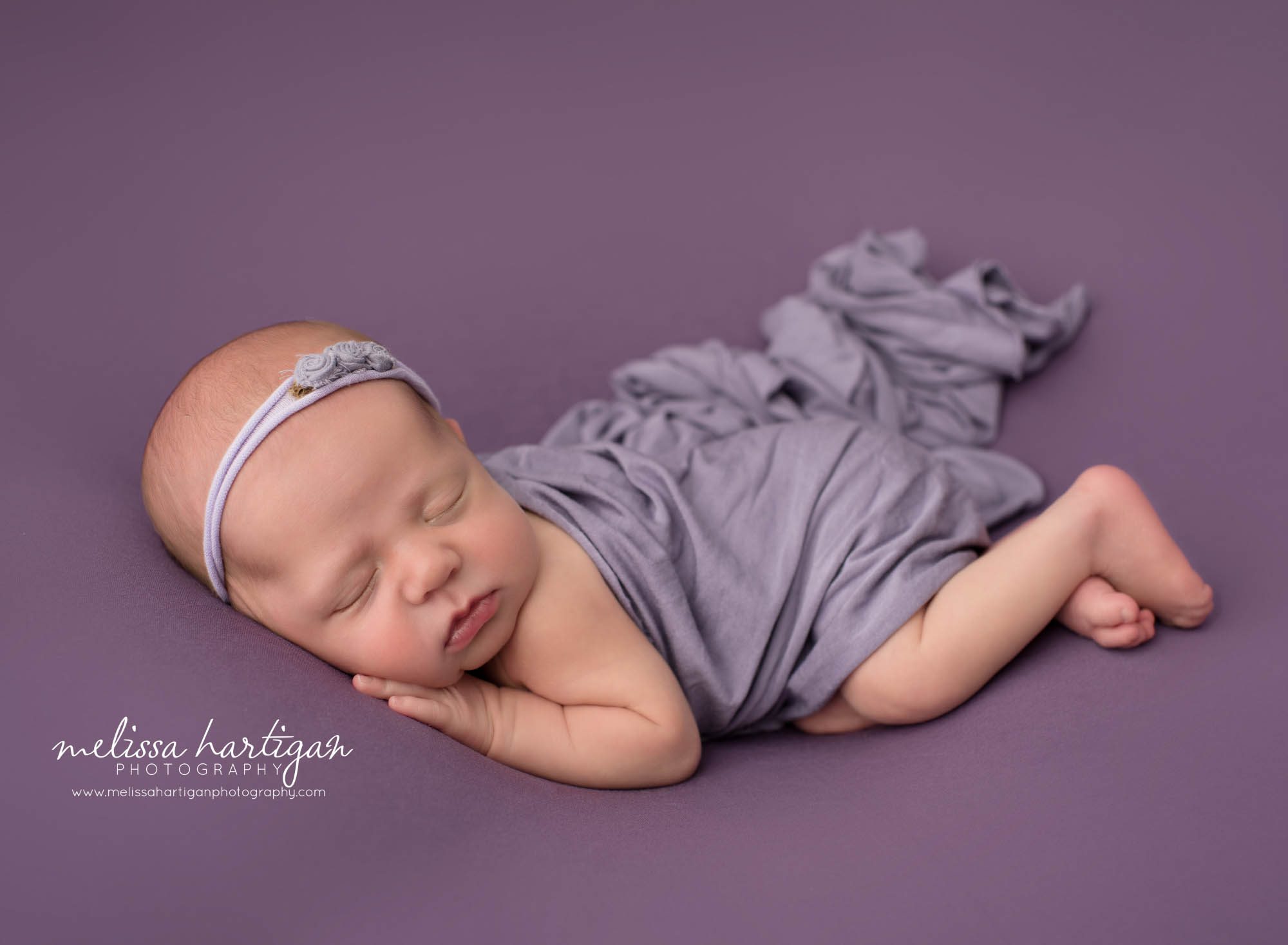 newborn baby girl posed on purple backdrop on side wearing floral headband newborn photographer Litchfield county ct