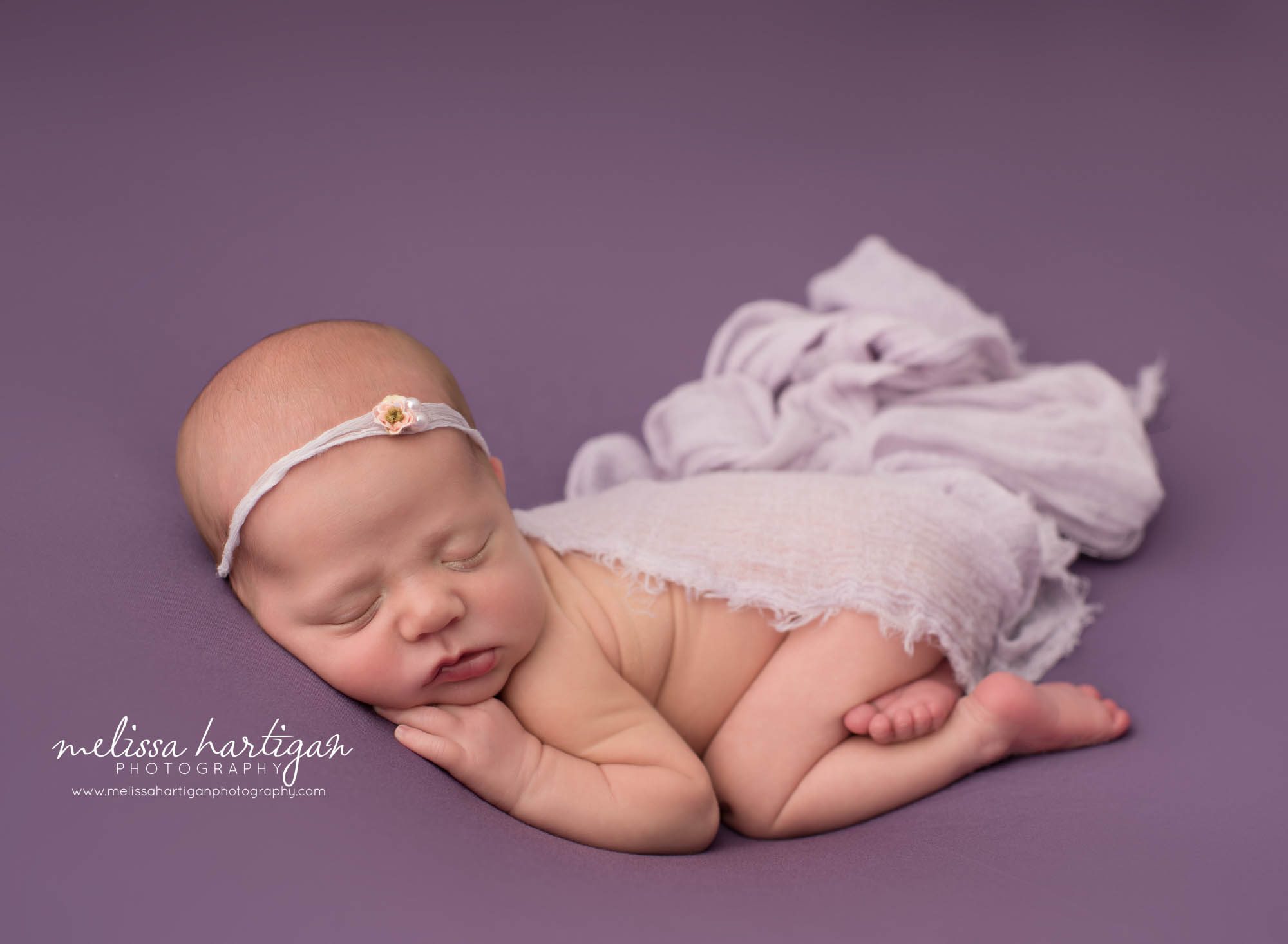 newborn baby girl posed on purple backdrop wearing light purple draping layer