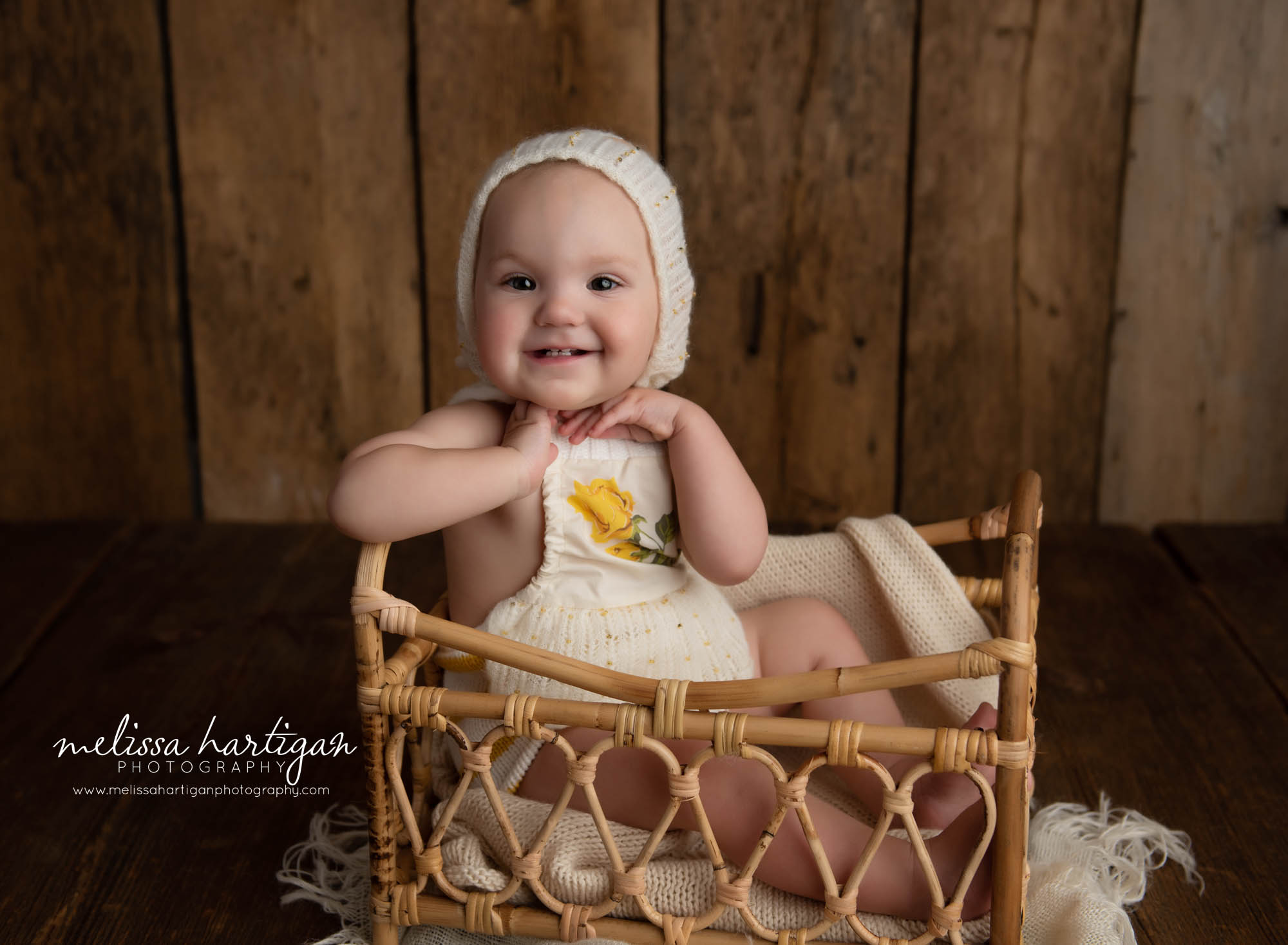 happy baby girl wearing knitted baby bonnet sitting in basket one year milestone photoshoot