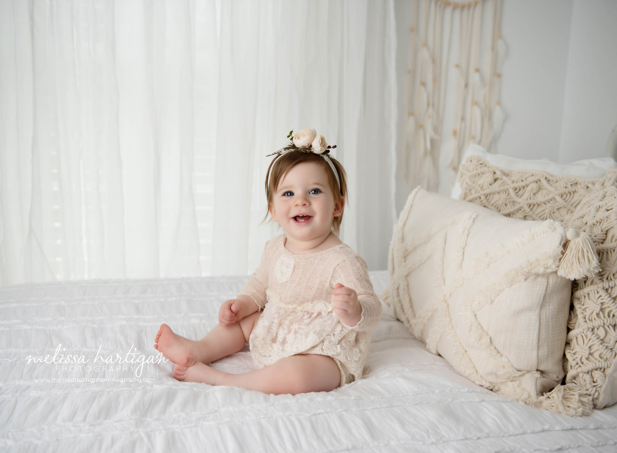 baby girl sitting happy on bed in photography studio during milestone photoshoot