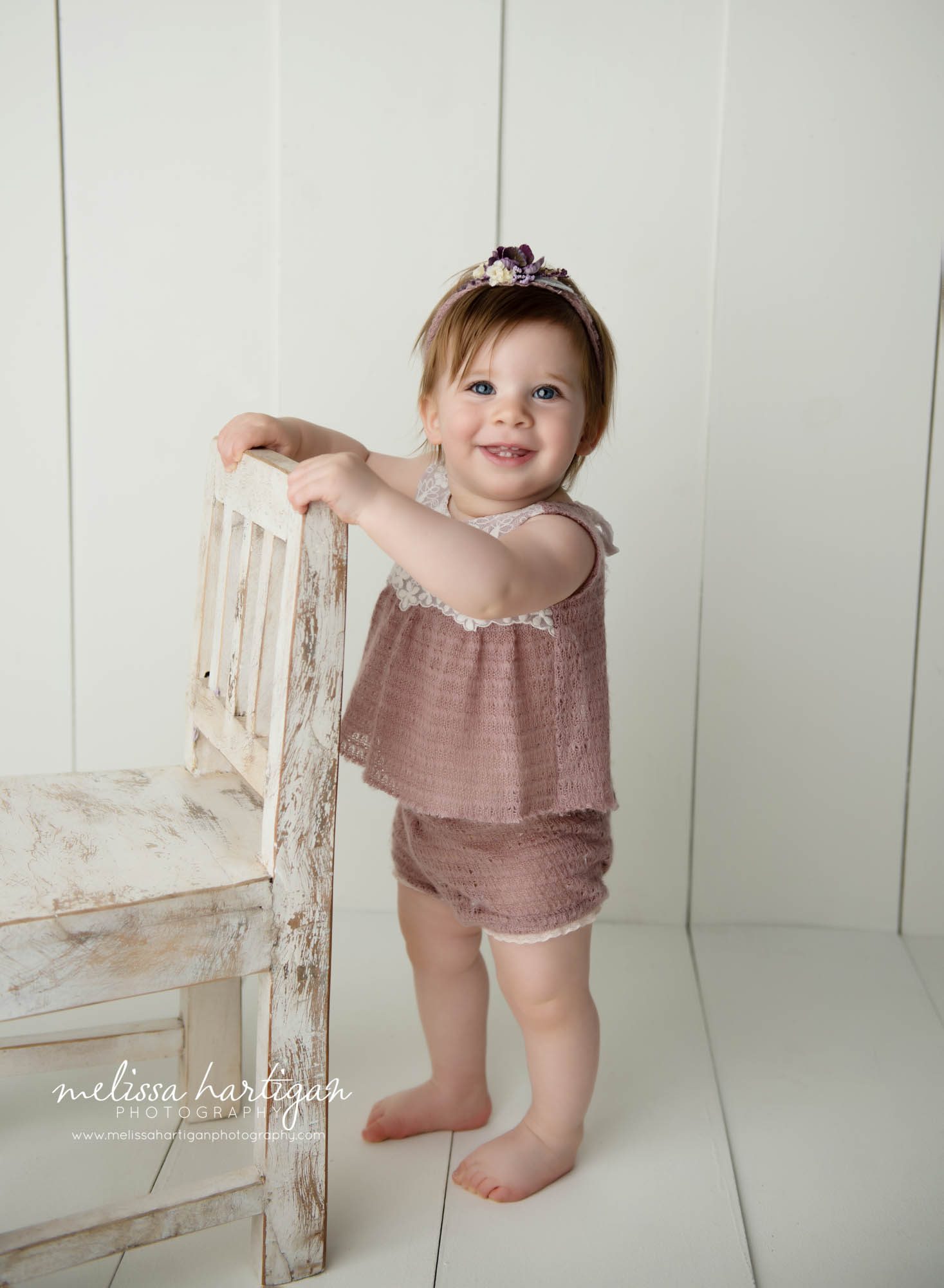 baby girl standing up smiling holding onto wooden chair in CT baby photography studio