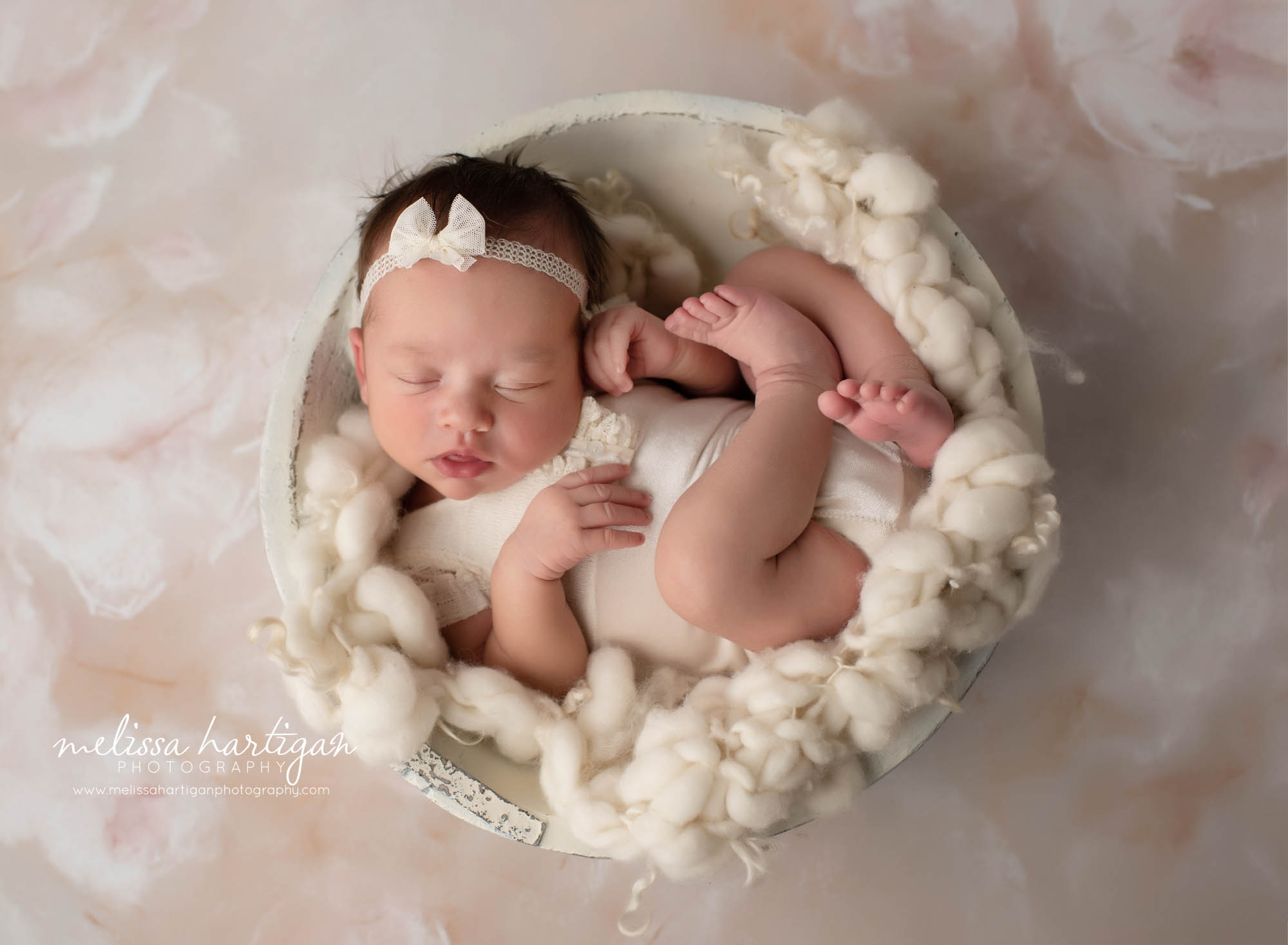 newborn baby girl waring cream outfit posed in wooden cream bowl with cream colored layer fluff