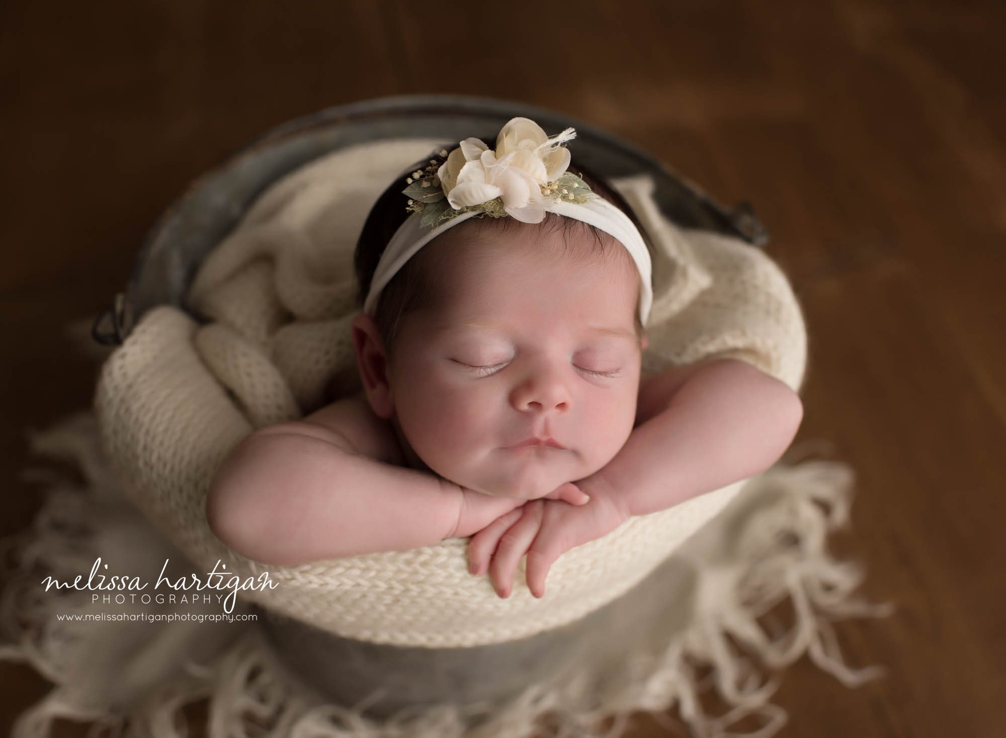 newborn baby girl posed in bucket with neutral beige knitted wrap wearing floral headband CT newborn photography