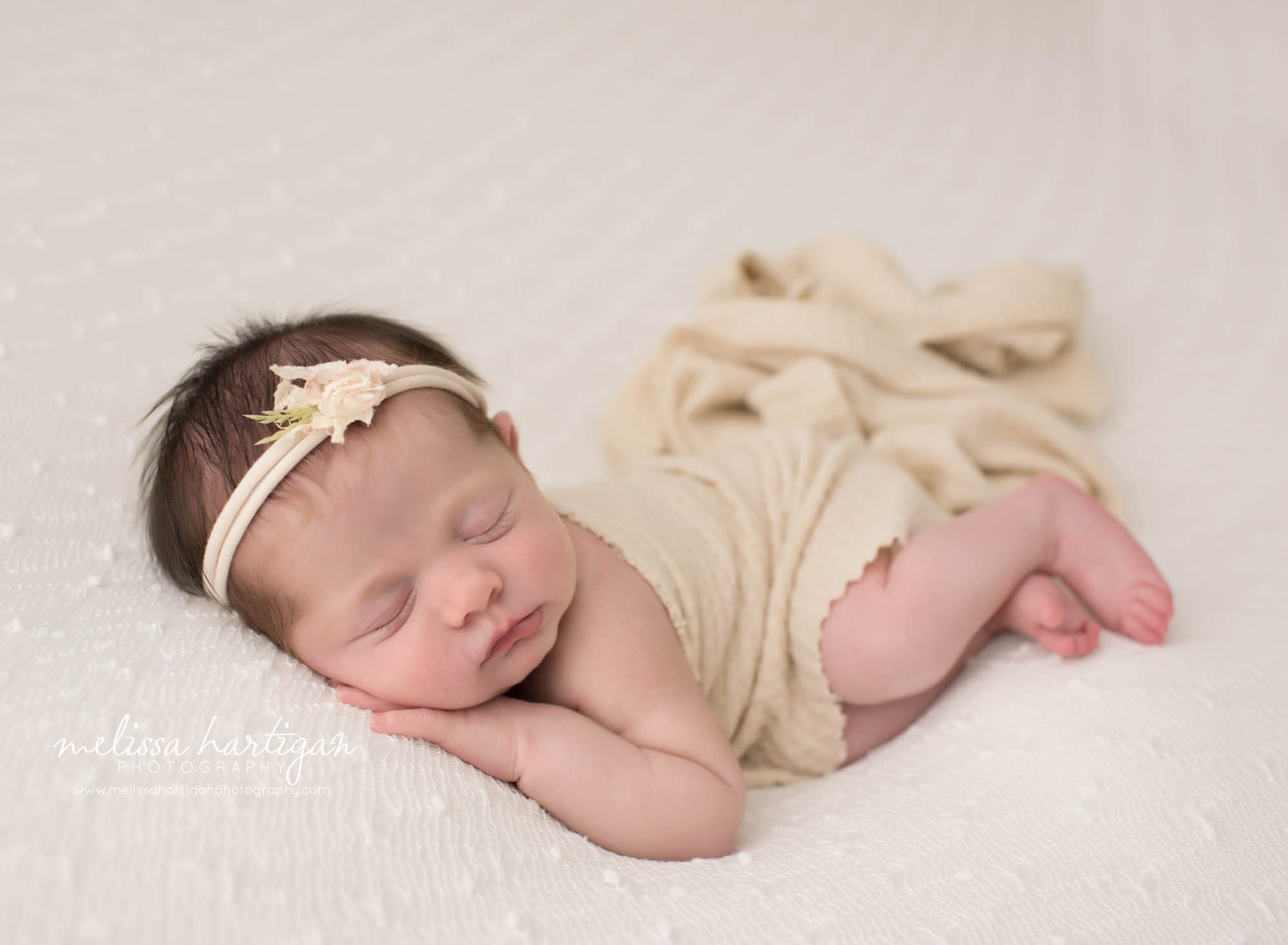 newborn baby girl posed on side with hand under cheek wearing headband and beige layer draped over her back colchester newborn photography