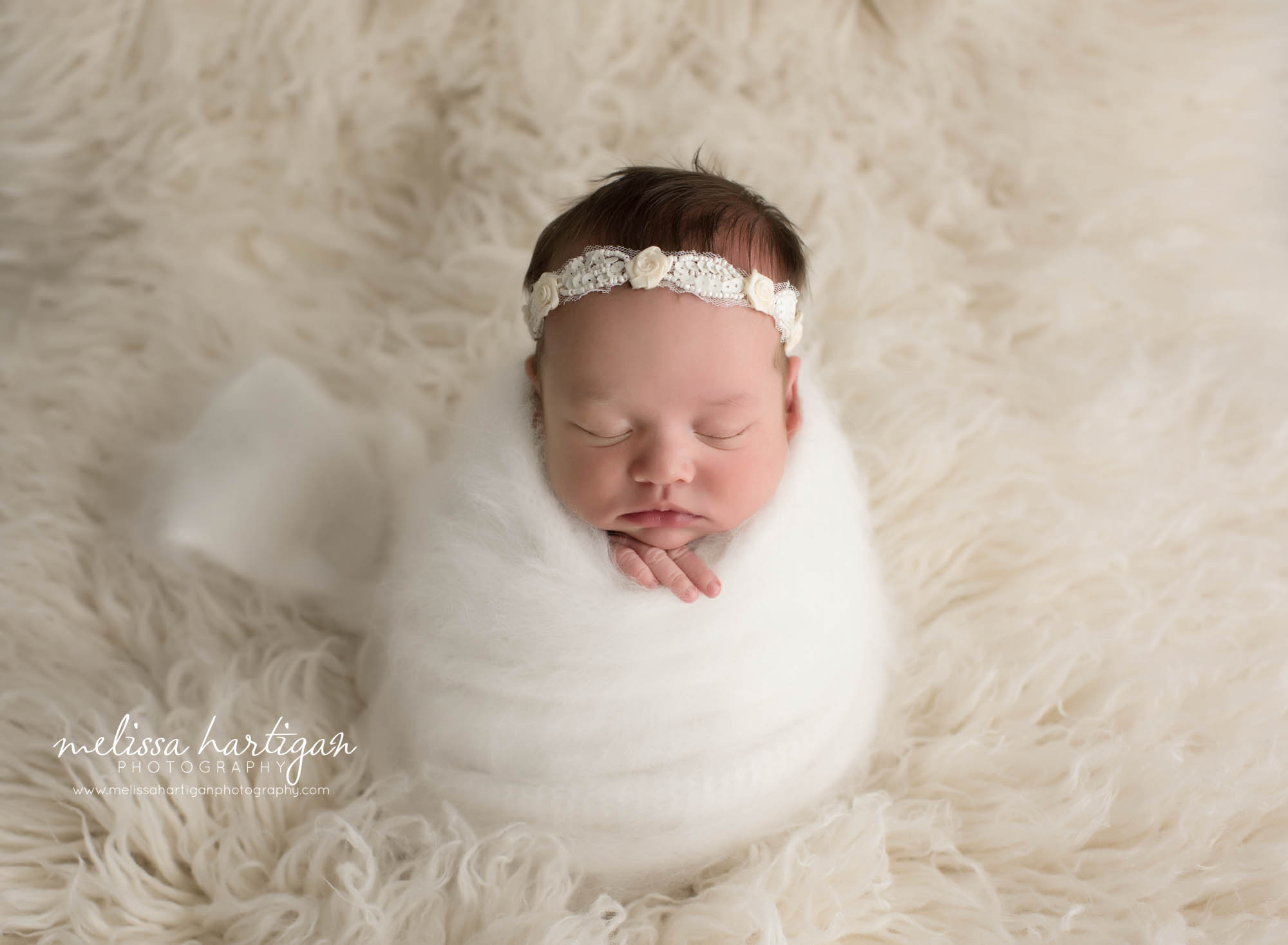newborn baby girl wrapped in white knitted angora wrap wearing headband