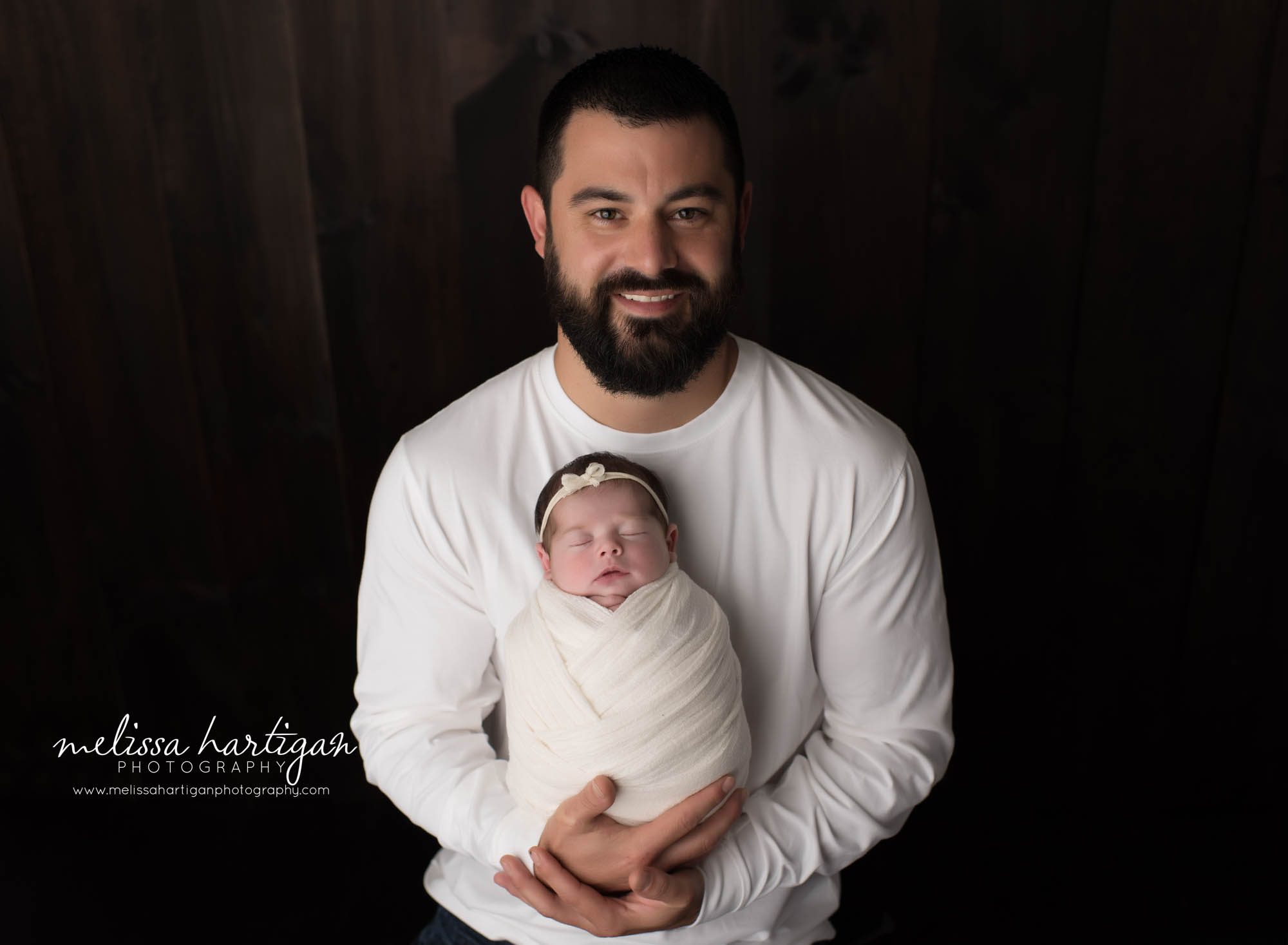 dad holding newborn daughter swaddled in cream wrap