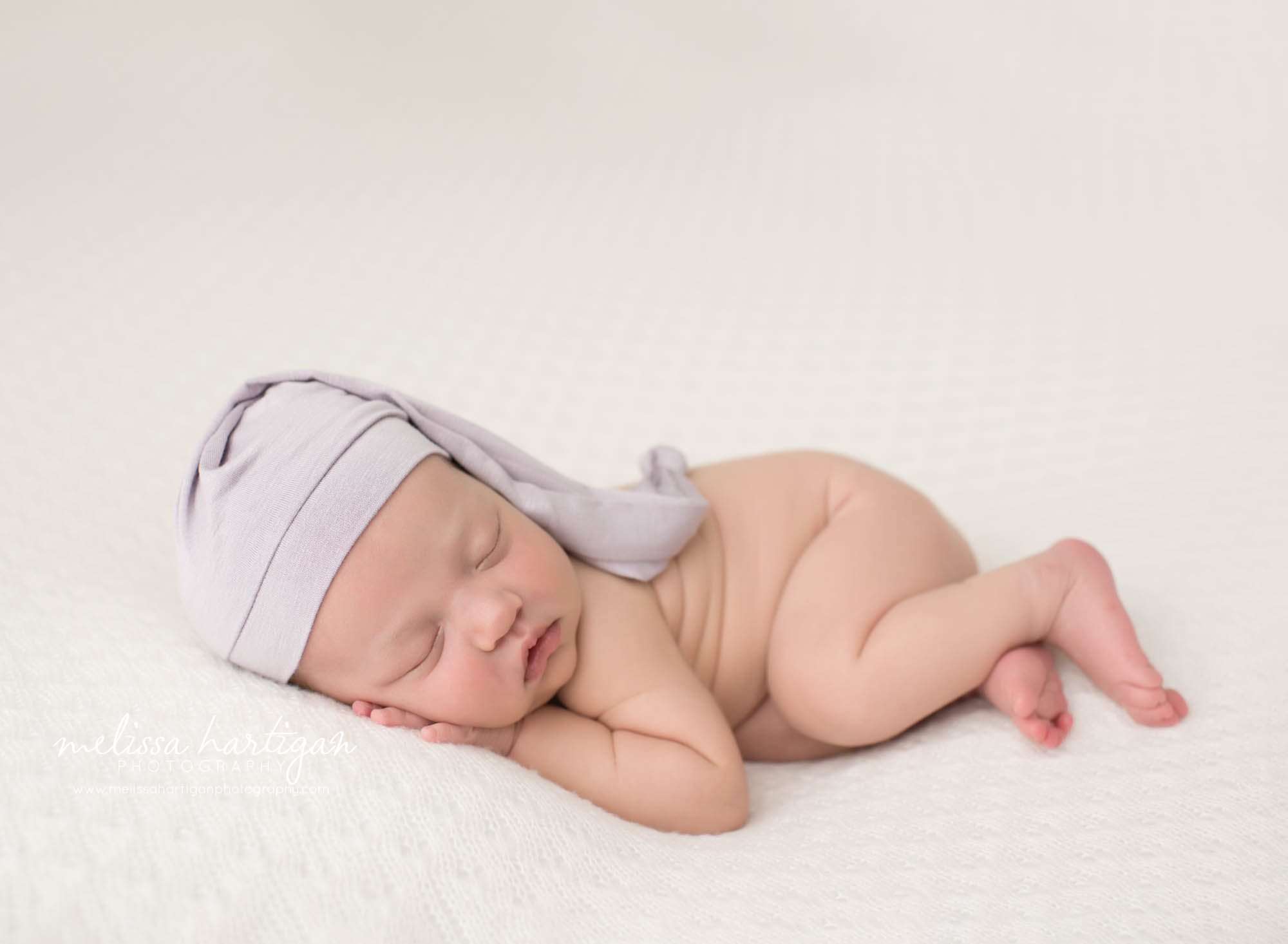 newborn baby girl posed on side wearing purple sleepy cap