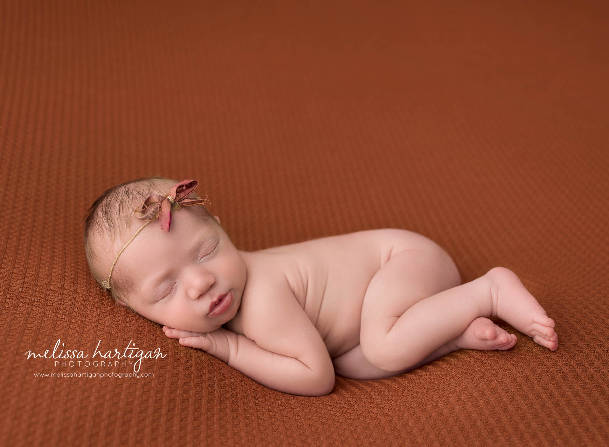 newborn baby girl posed on side tummy wearing bow headband