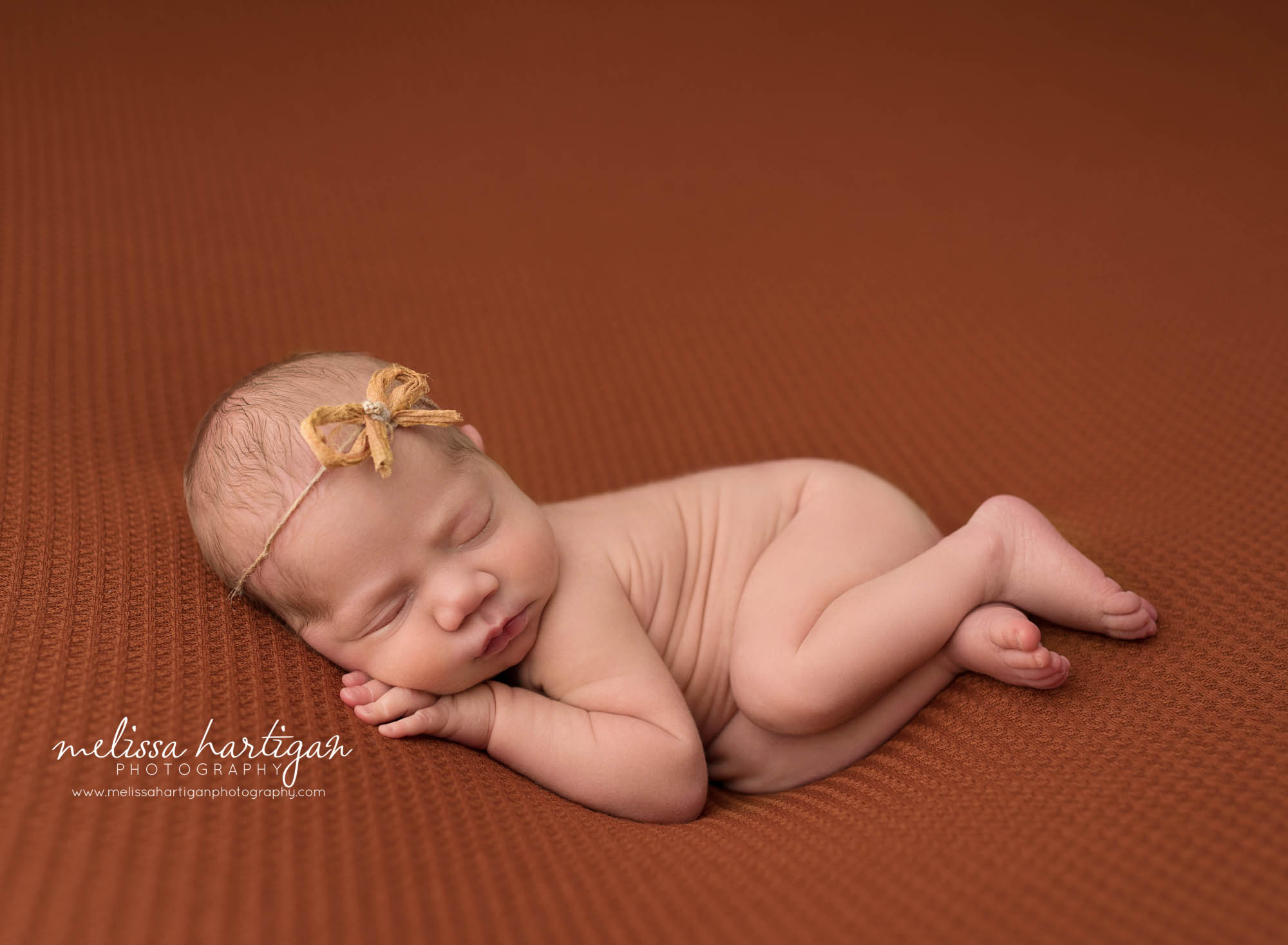 newborn baby girl posed on side with hand under cheek wearing bow headband west hartford CT baby photography