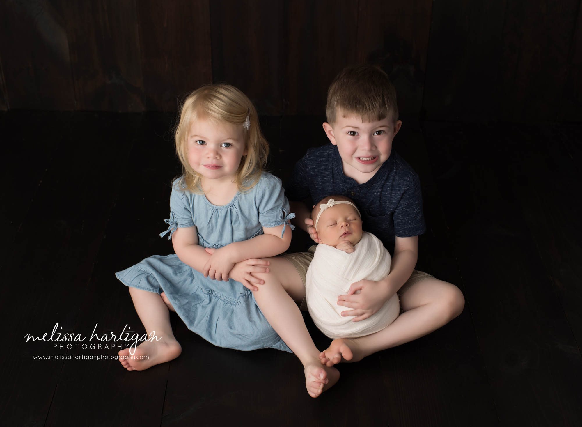 newborn baby girl wrapped posed with two older siblings holding her