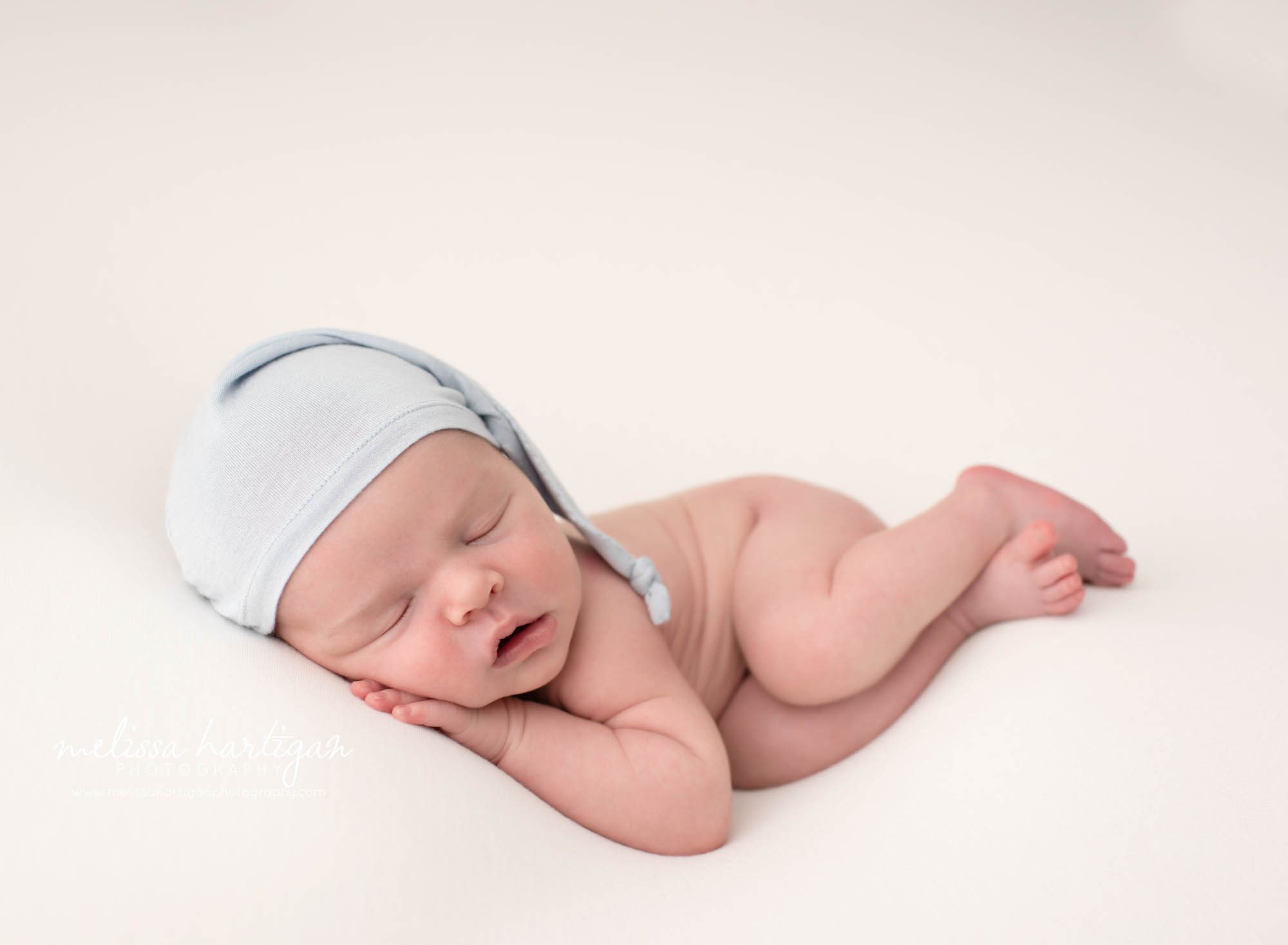 newborn baby boy posed on side wearing light blue sleepy cap sleeping peacefully