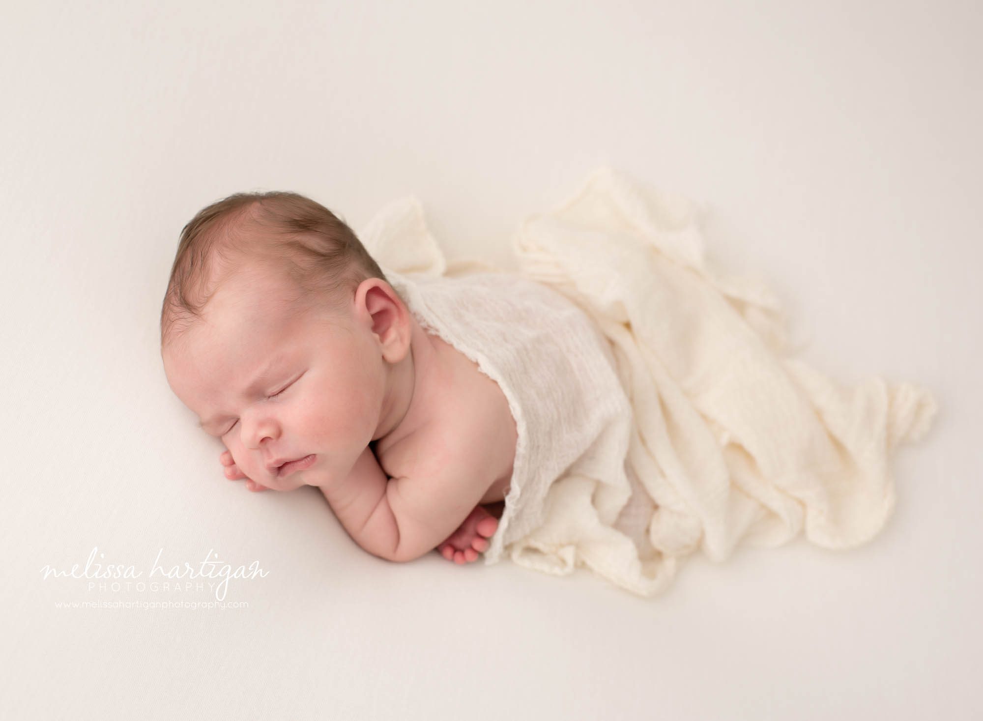 newborn baby boy posed modified taco pose with cream layer draped over back