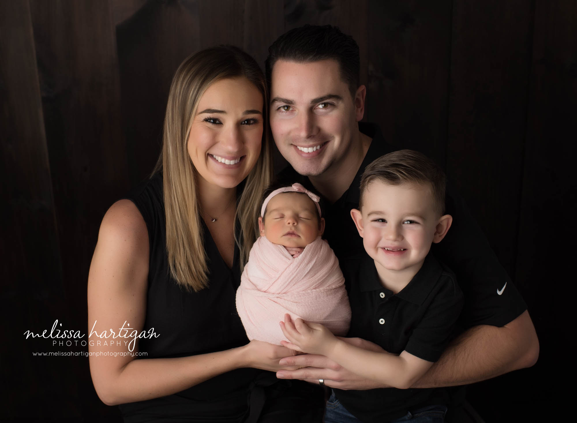 newborn baby girl wrapped in pink wrap held by mom dad and big brother for family pose