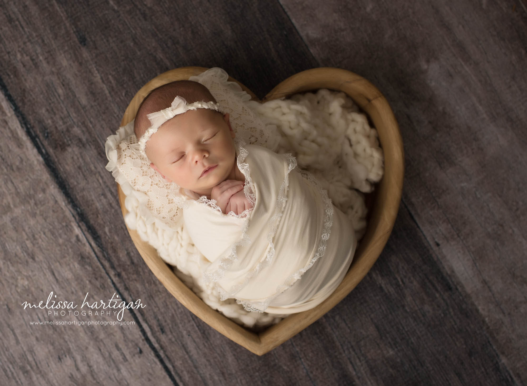 newborn baby girl wrapped in cream lace wrap posed in wooden heart bowl prop