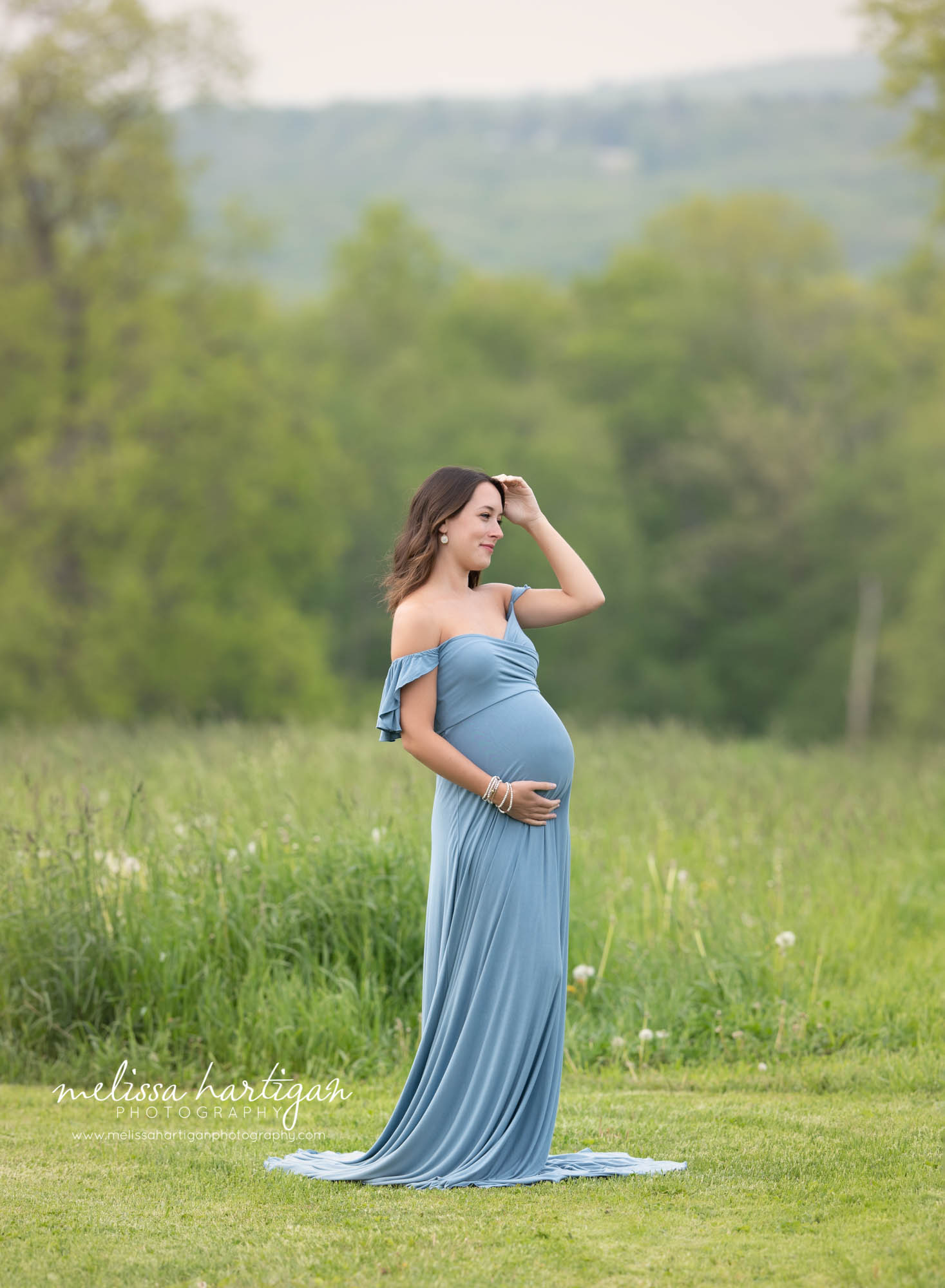 mom brushing hair off her face holding baby bump during maternity photoshoot
