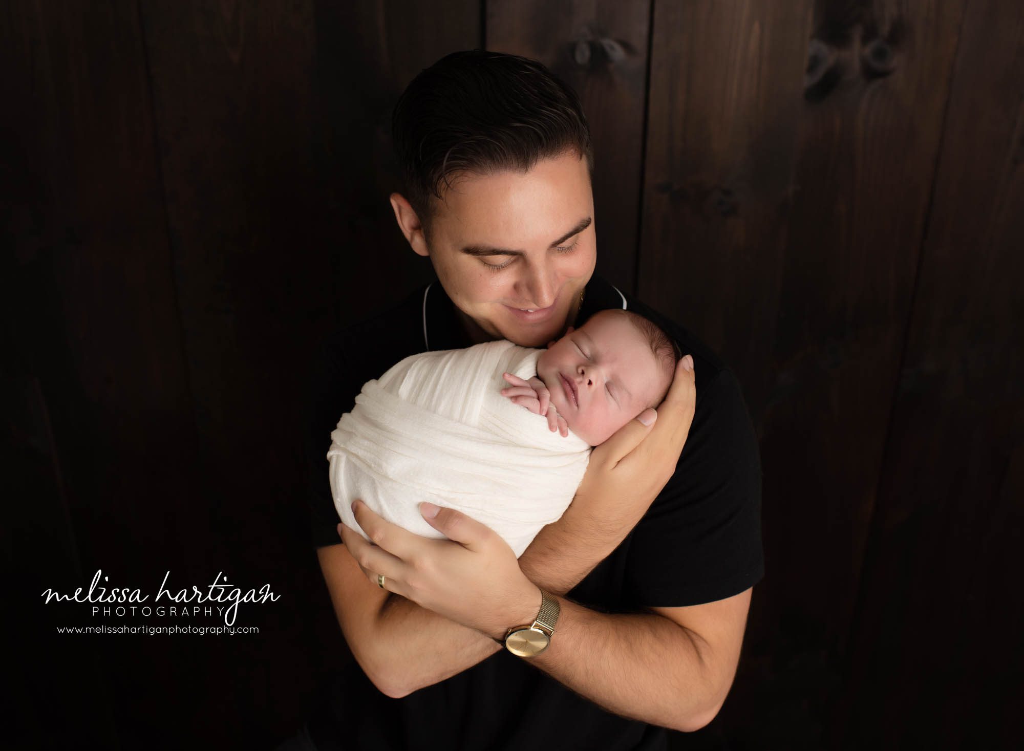 dad looking down happy holding newborn son wrapped in cream wrap in parents pose newborn photography photoshoot in coventry CT
