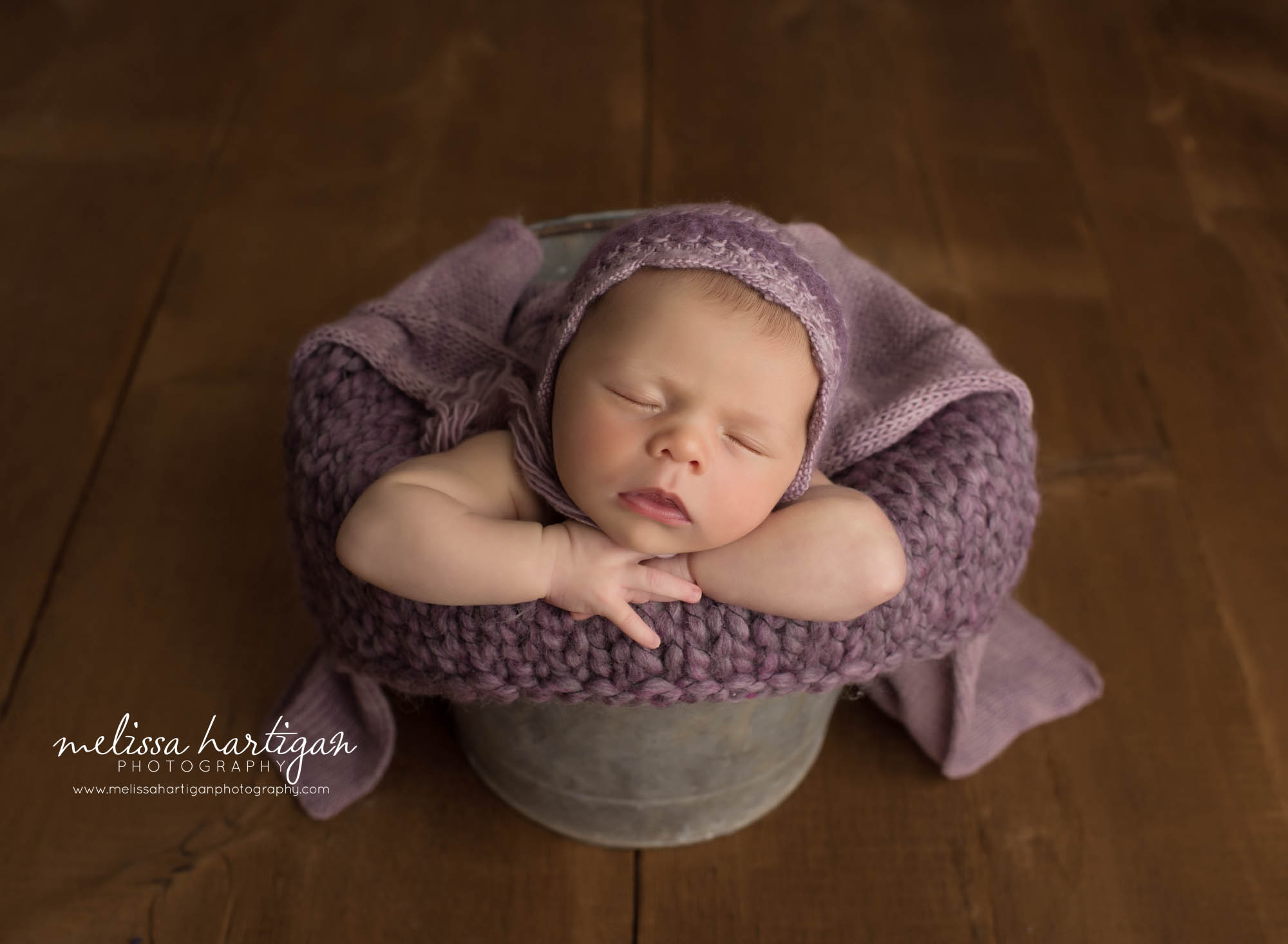newborn baby girl posed in bucket wearing purple bonnet Connecticut newborn photographer