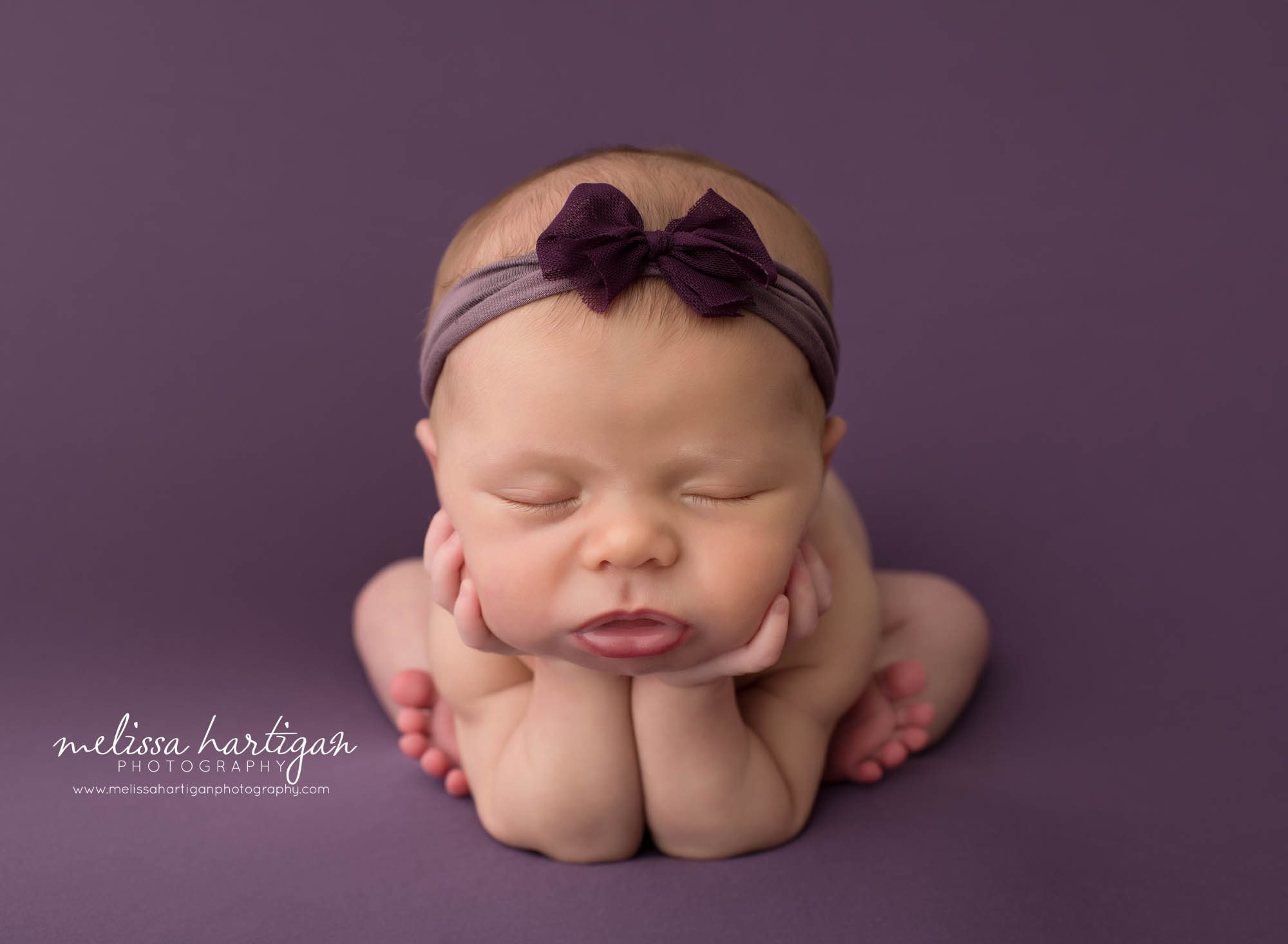 newborn baby girl posed froggy pose on purple backdrop
