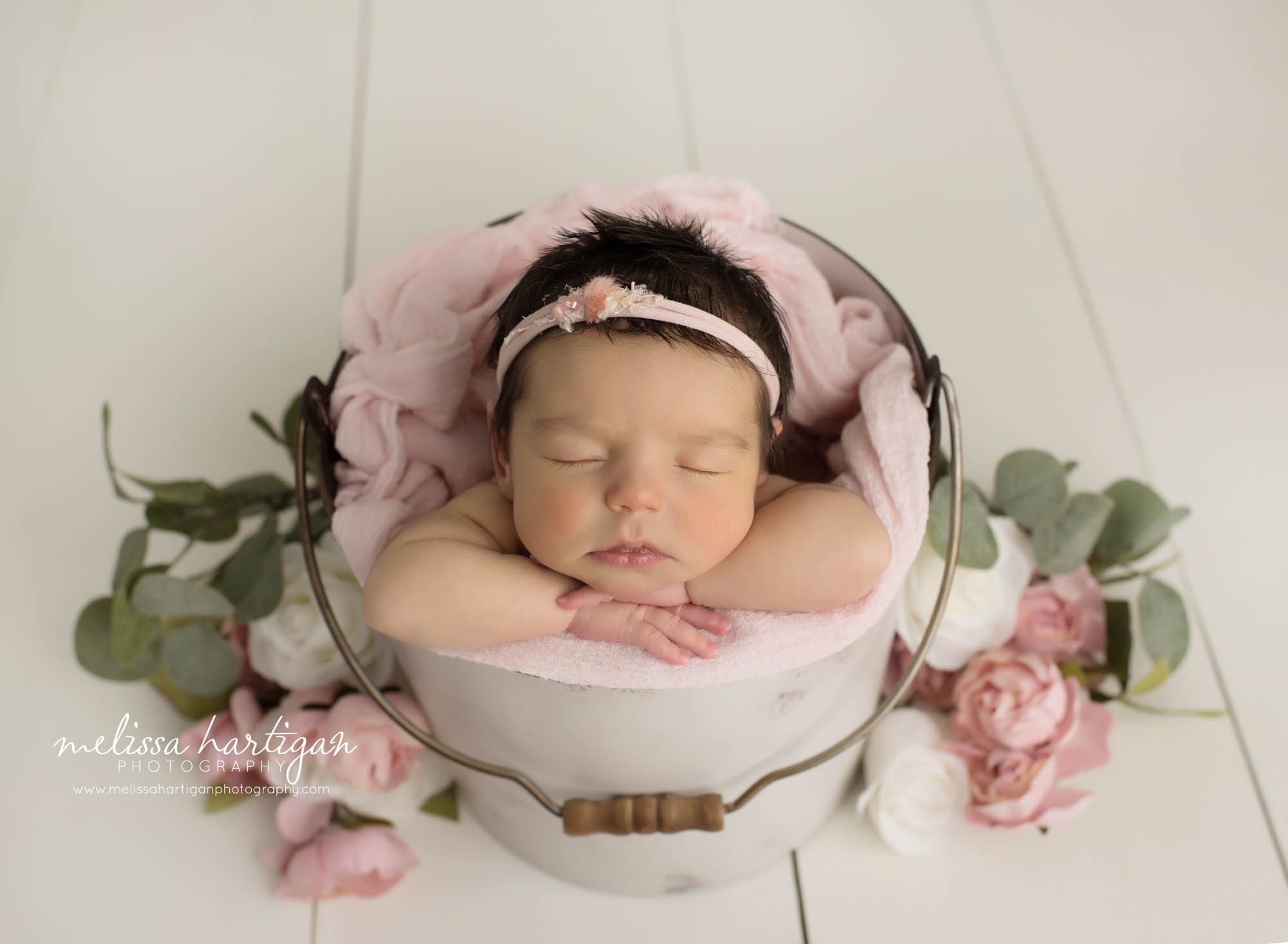 newborn baby girl posed in bucket with pink flowers